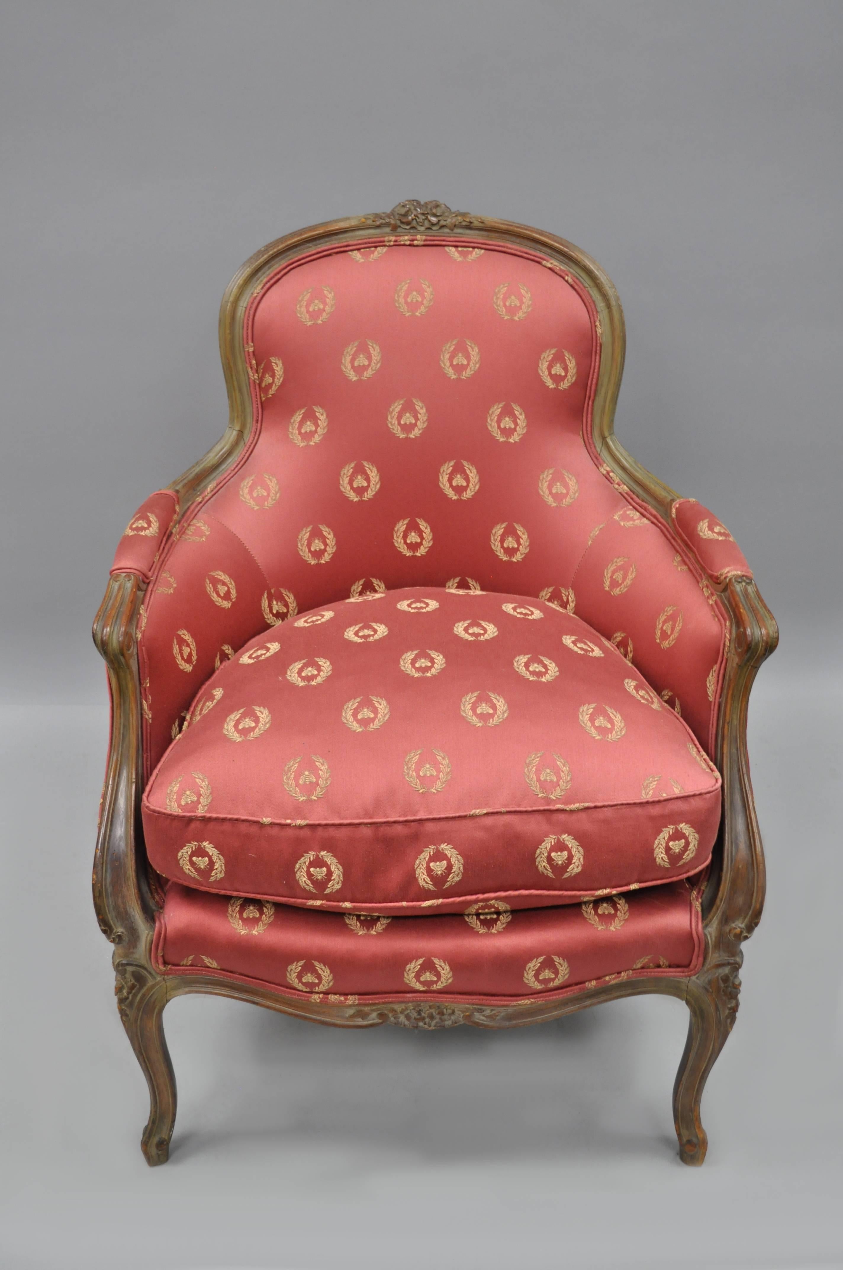 Antique French country / Louis XV style Bergere armchair. Chair features upholstered armrests, floral carved top tail, cabriole legs, and a desirable antiqued / distressed finish to the solid wood frame.