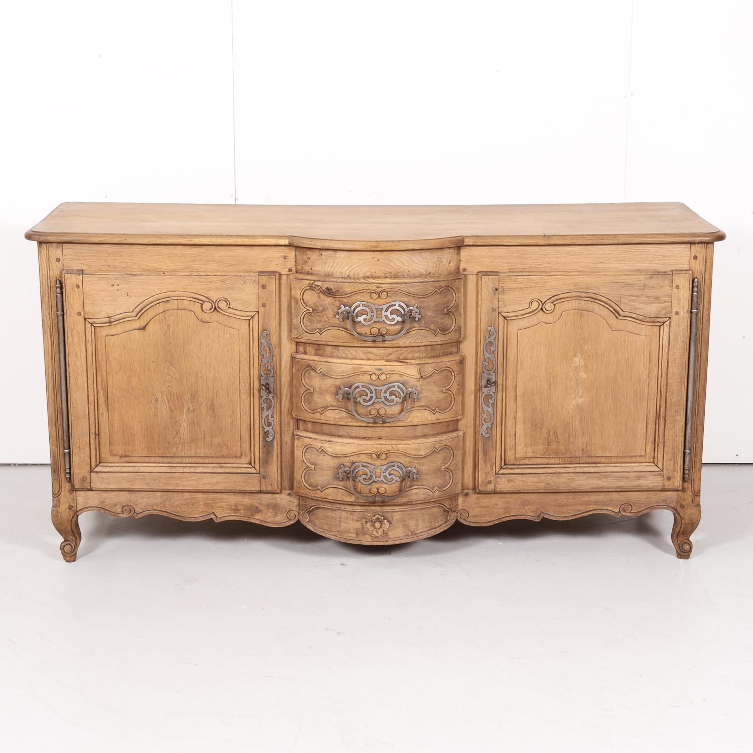 A beautiful antique French Country Louis XV style bleached oak bow front enfilade buffet from Bordeaux having a center tier of three drawers in a bow front shape stacked one upon the other flanked by carved panel doors that open to reveal a single