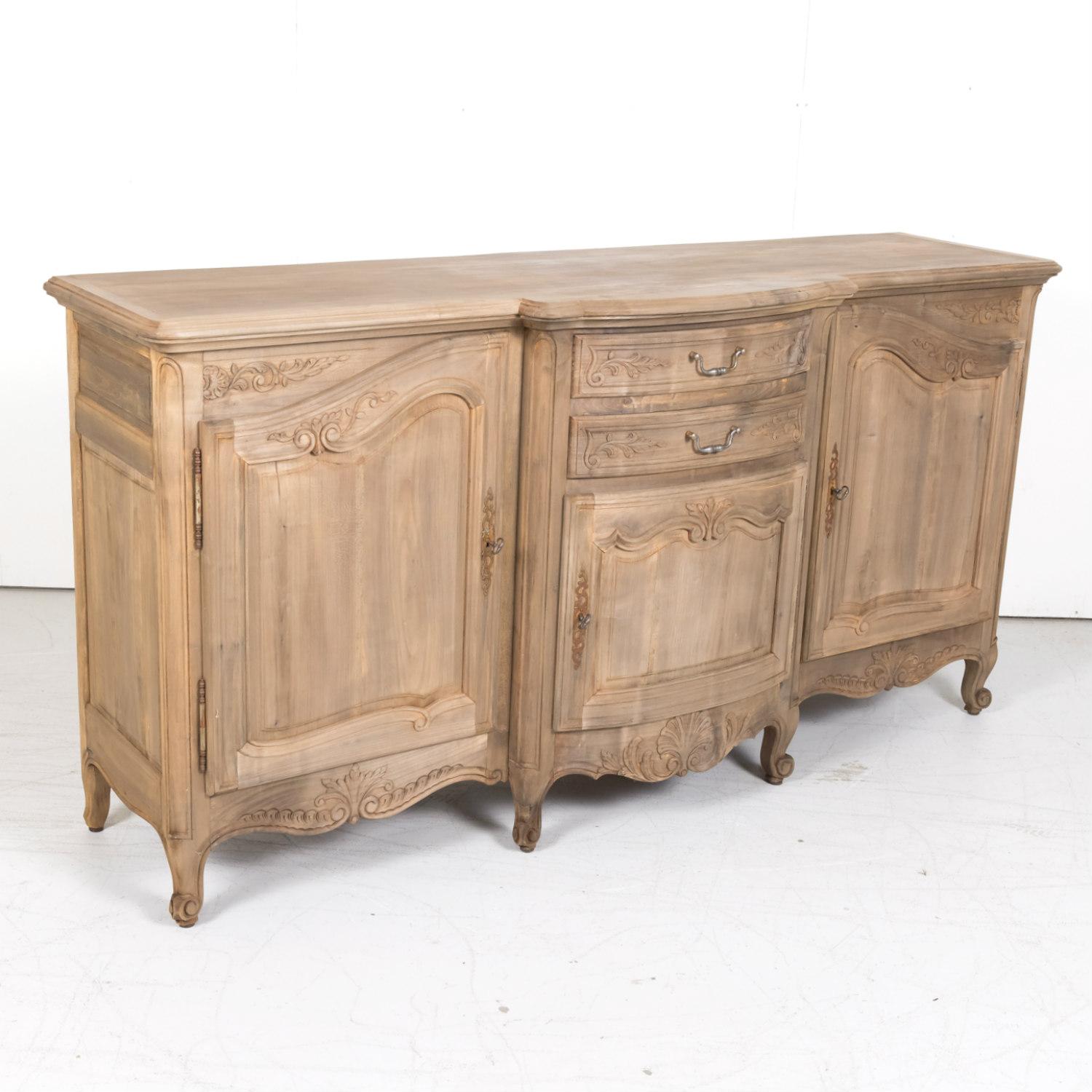 Antique French Country Louis XV style bleached walnut enfilade buffet from Lyon, circa 1920s, having two center drawers in a bow front shape stacked one upon the other over a small center carved panel door all flanked by large carved panel doors