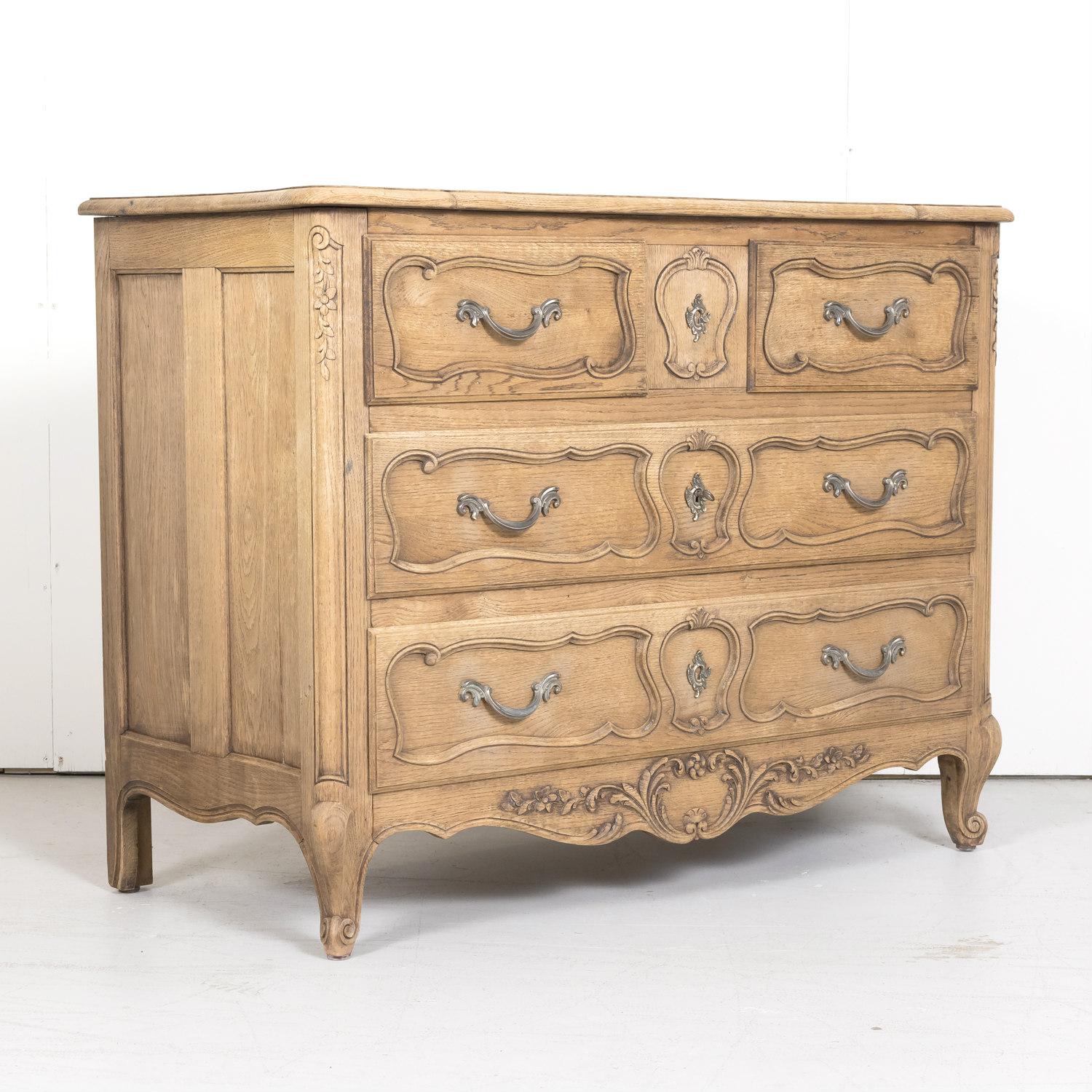 Antique French Country Louis XV style four-drawer commode handcrafted in Normandy of old growth oak that's been bleached or washed to a natural finish retaining its beautiful patina, circa 1900s, having a beautifully carved serpentine top above two