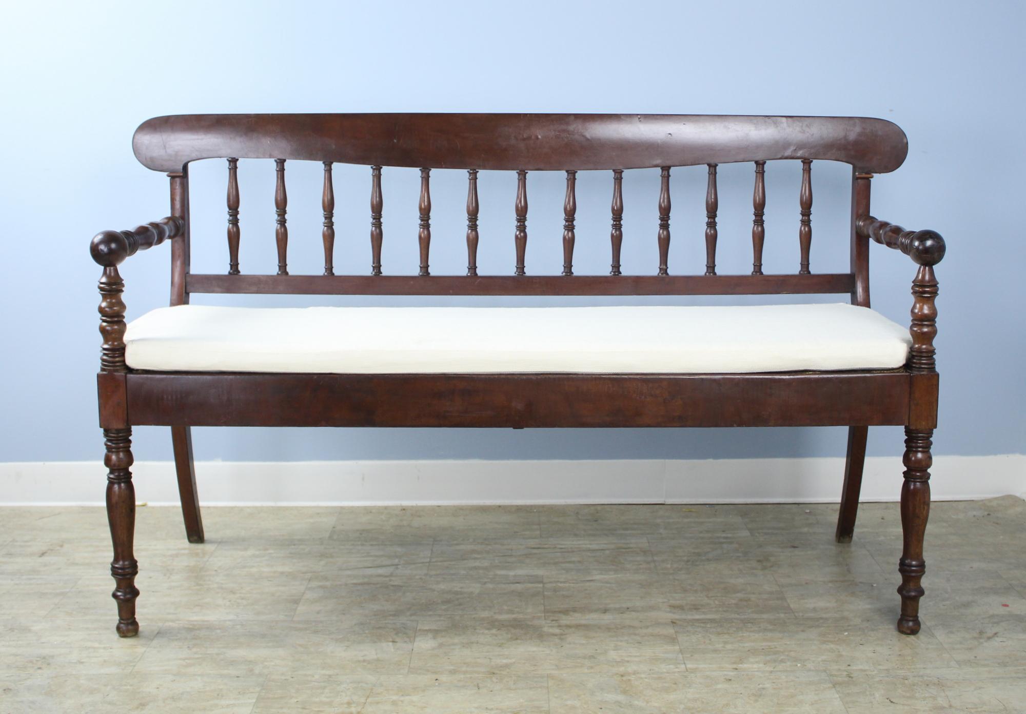 A splendid French bench in dark glossy mahogany. Charming spindle back and turned front legs are accented by graceful flared back legs.  There are some small areas of wear on the backrest.   Sturdy and comfortable, with new strapping supports and