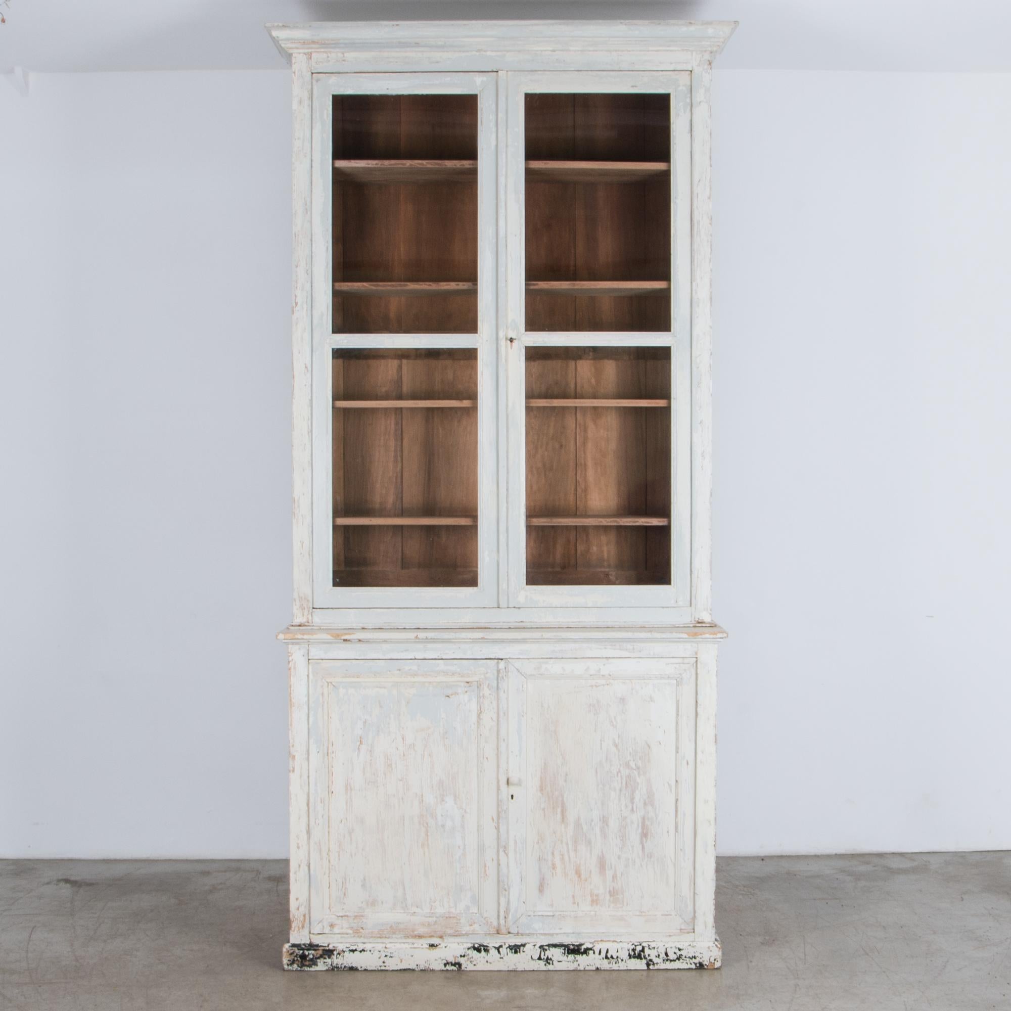 Two lower doors and glass display windows give this piece potential for storage or display. From France, circa 1900, a simple geometric shape recalls a countryside local in a pale cool white, gently distressed. Distinctive period design is