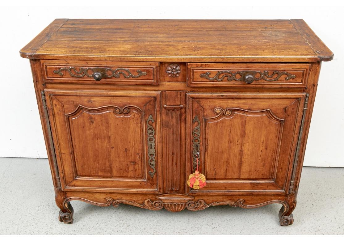 An early French Server in Classic French Country Style. A useful medium size elegant cabinet with bread board plank constructed top. The two apron drawers decorated with applied foliate scrolled metal plaques and knob pulls, flanking a carved