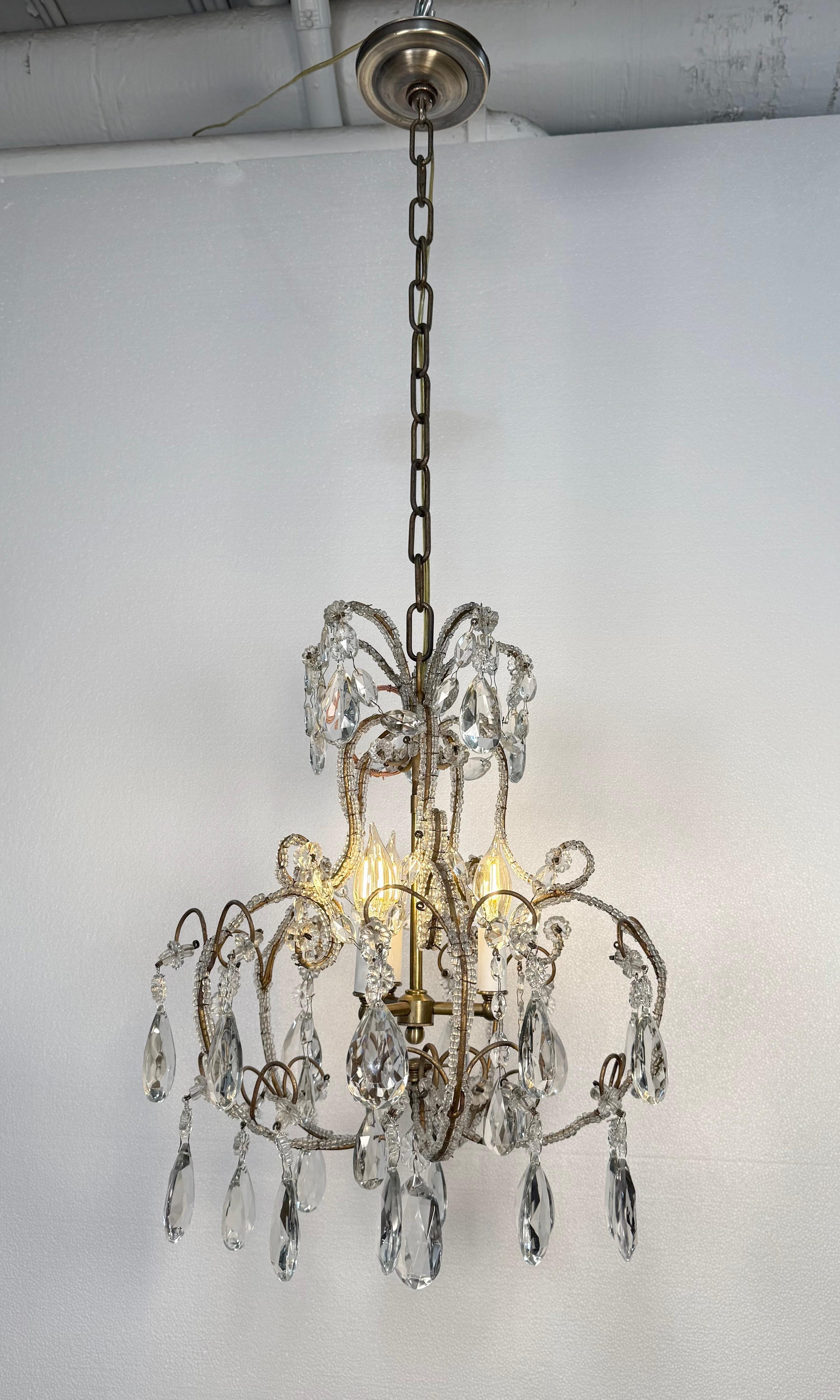 French style basket chandelier with draped teardrop shaped faceted crystals topped with florets and accented with round bead shaped crystals attached to the frame. The frame is made of brass. This light requires three candelabra light bulbs. Good
