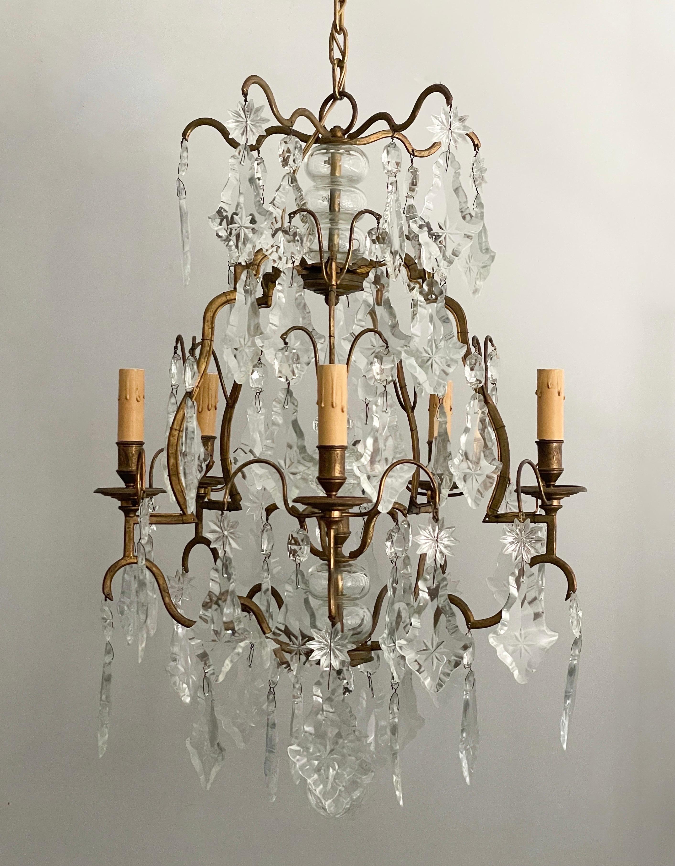 Gorgeous, French 1940s crystal chandelier in the Versailles-style. 

This chandelier features a scrolled gilt-brass frame heavily adorned with etched crystal prisms and stars. 

The chandelier is wired and in working condition, it requires 5
