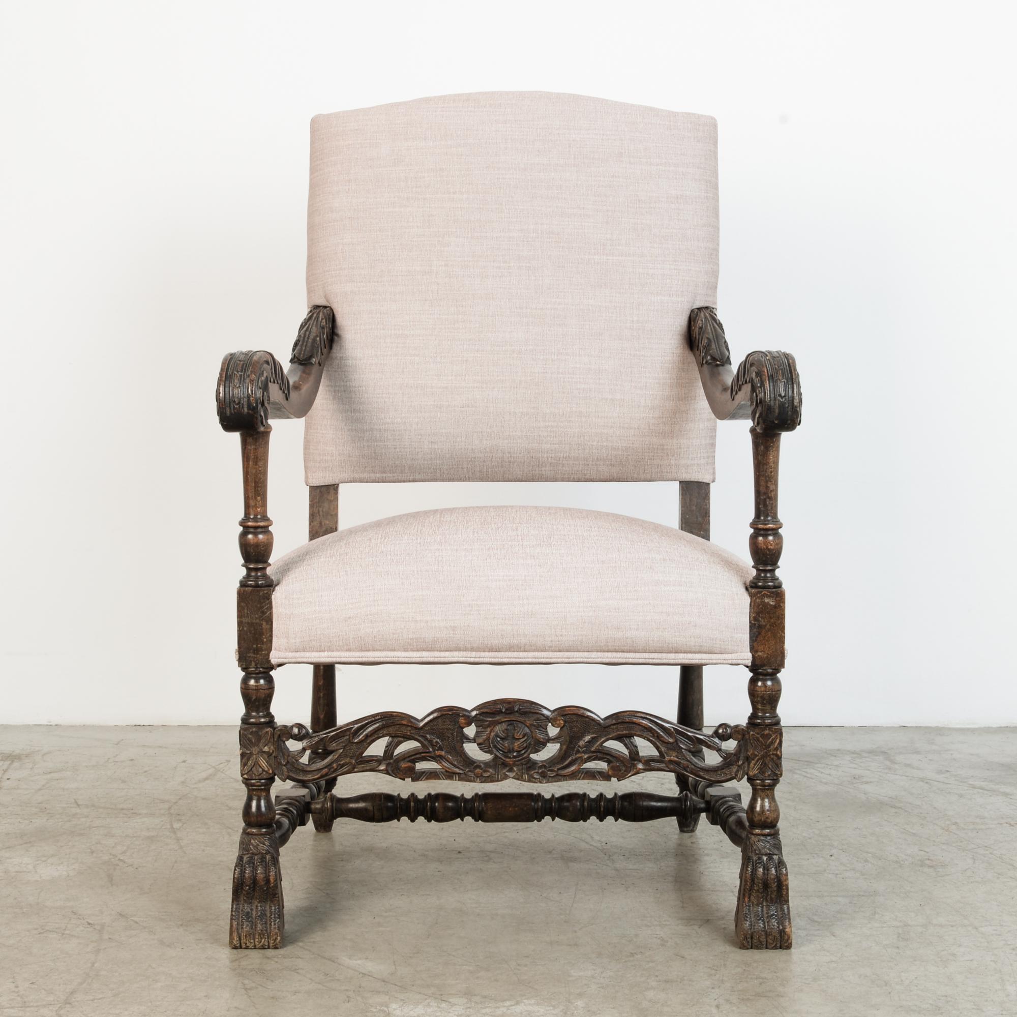 Ornate upholstered armchair from France, circa 1900. This chair features elaborate carved armrests, with clawfoot legs and floral details in dark stained oak. With comfortable grey cotton-linen upholstery, this chair is fitted for contemporary