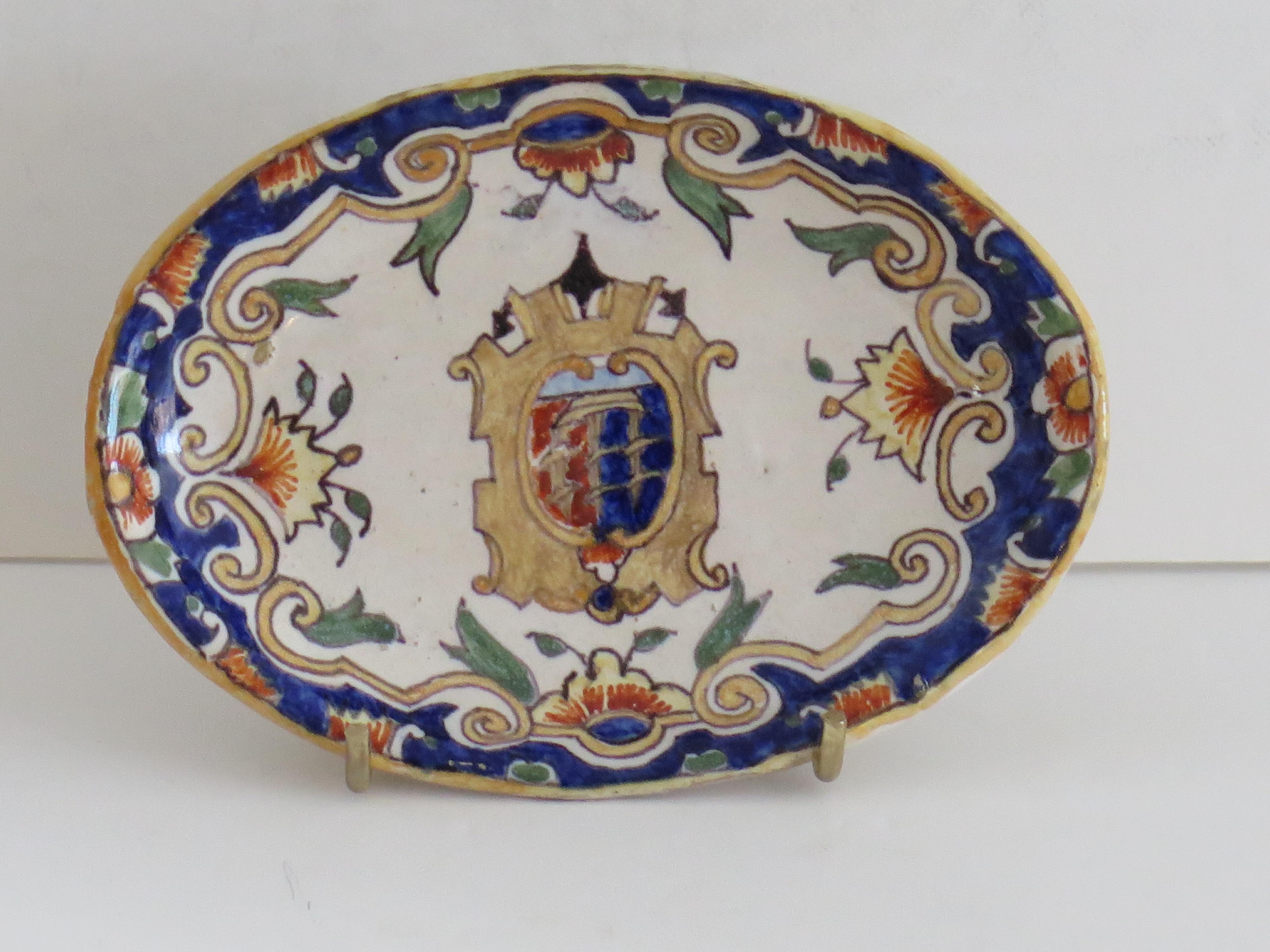 This is a very interesting Faience dish, made in Dieppe, Northern France during the second half of the 19th century.

The dish is fairly small with an oval shape and raised on a low foot.
It is all hand painted with an armorial scene.

It is