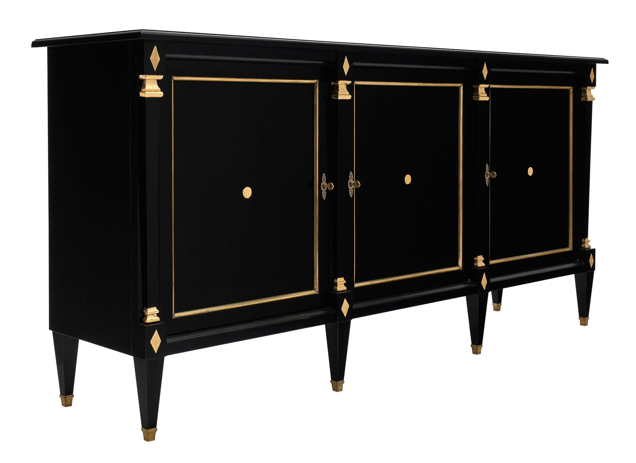 French Directoire antique buffet made of mahogany with filed brass trims throughout and gold leafed details. There are three doors with interior shelving. We love the strong tapered legs and ebonized French polish finish of this case piece.