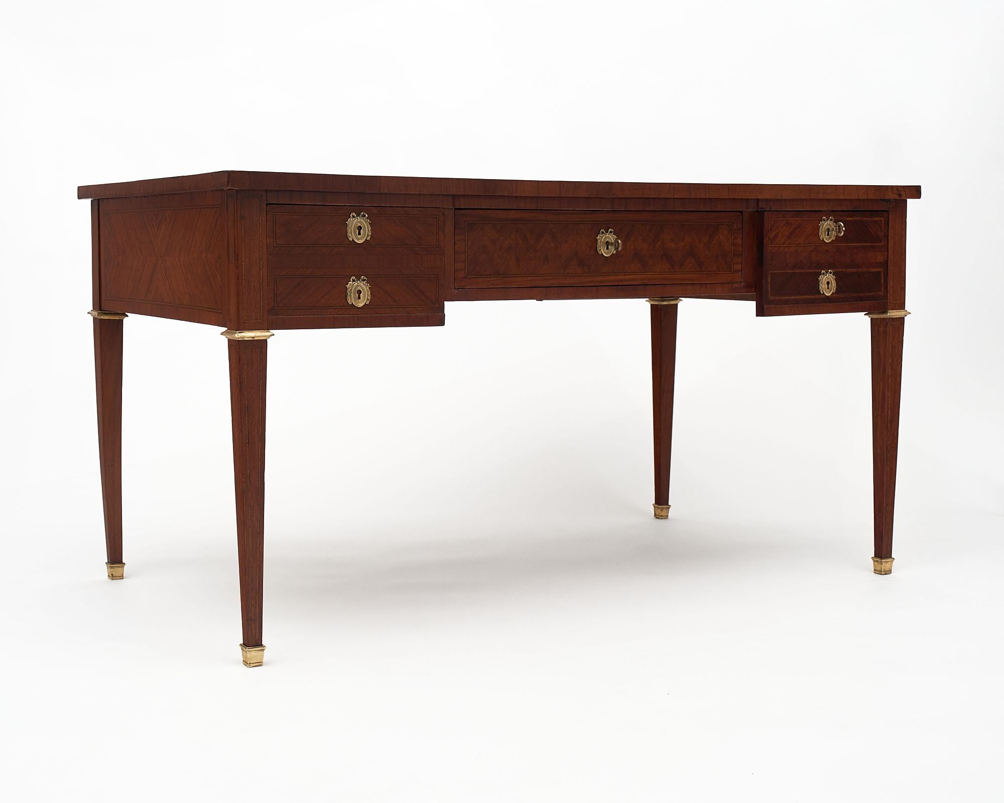 French burled ash desk in the Directoire style, finished in a lustrous museum quality French polish. This work table features five dovetailed drawers adorned with finely cast gilded bronze and a gilt embossed moleskin top.