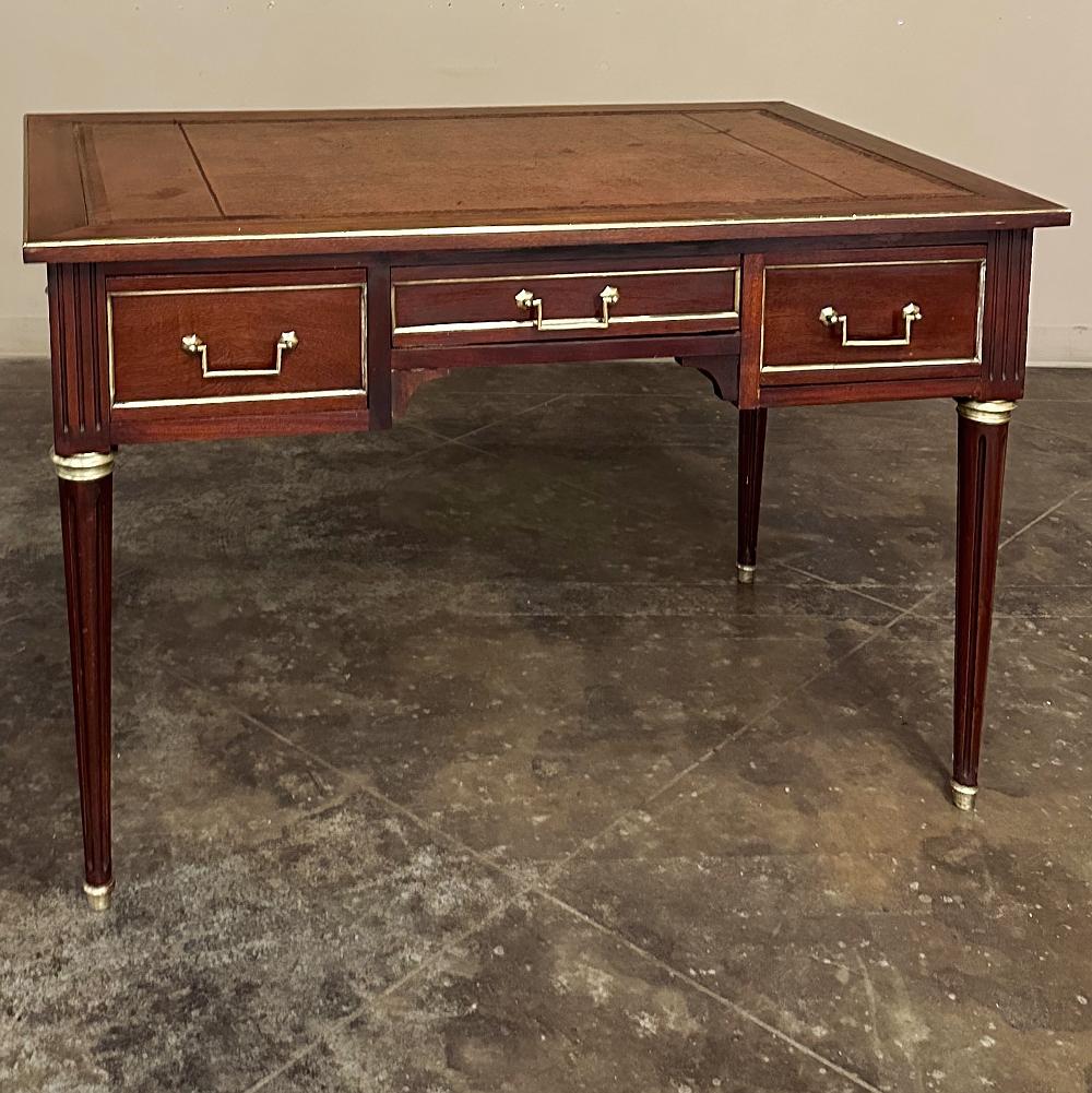 Antique French Directoire Neoclassical Mahogany Leather Top Desk is a marvel of timeless architecture, tailored styling and quality materials.  Crafted from exotic imported mahogany, the rich oxblood red tones of the wood exude richness.  Brass