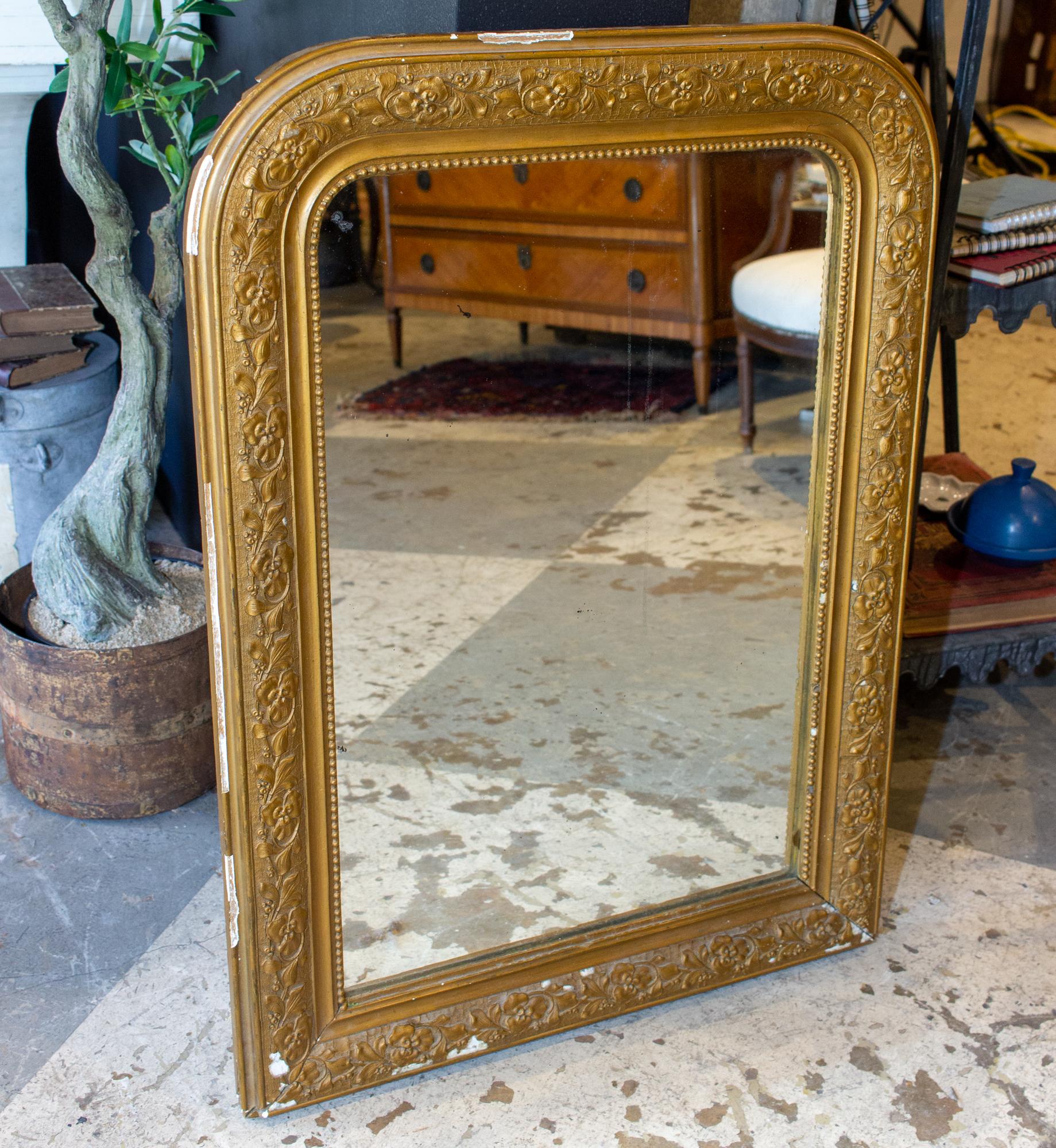 This antique French Louis Philippe mirror has a distressed gold finish with a raised floral pattern molding along the center of the frame and a beaded interior edge. The flowers appear to be pansies. Mirror is in good condition, with some spotting