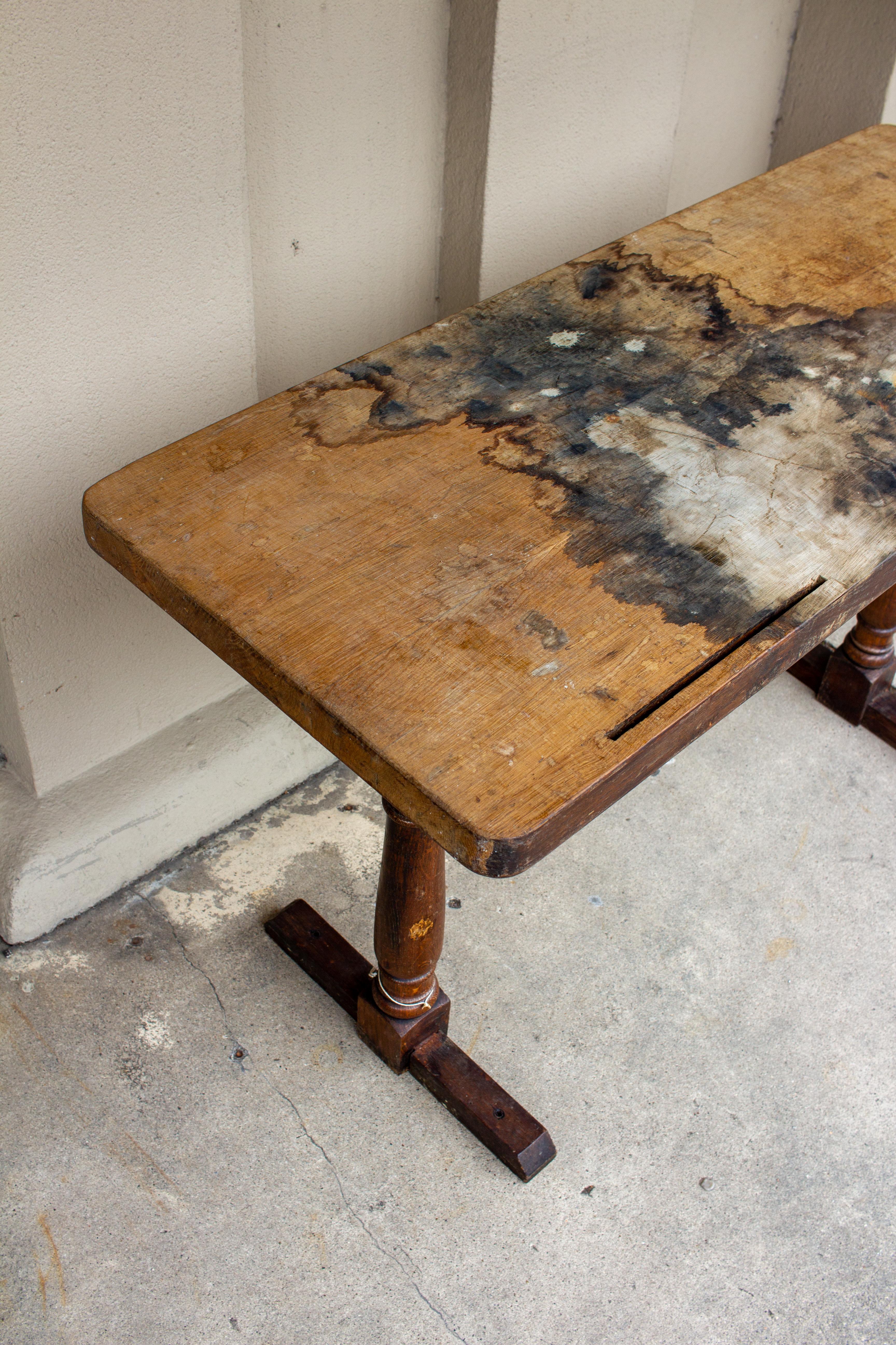 This antique French wooden console is a two-piece table with a base featuring turned details in the legs and a very distressed top. The top also has slots on one end that may have held another piece at one time, but it is uncertain what it might