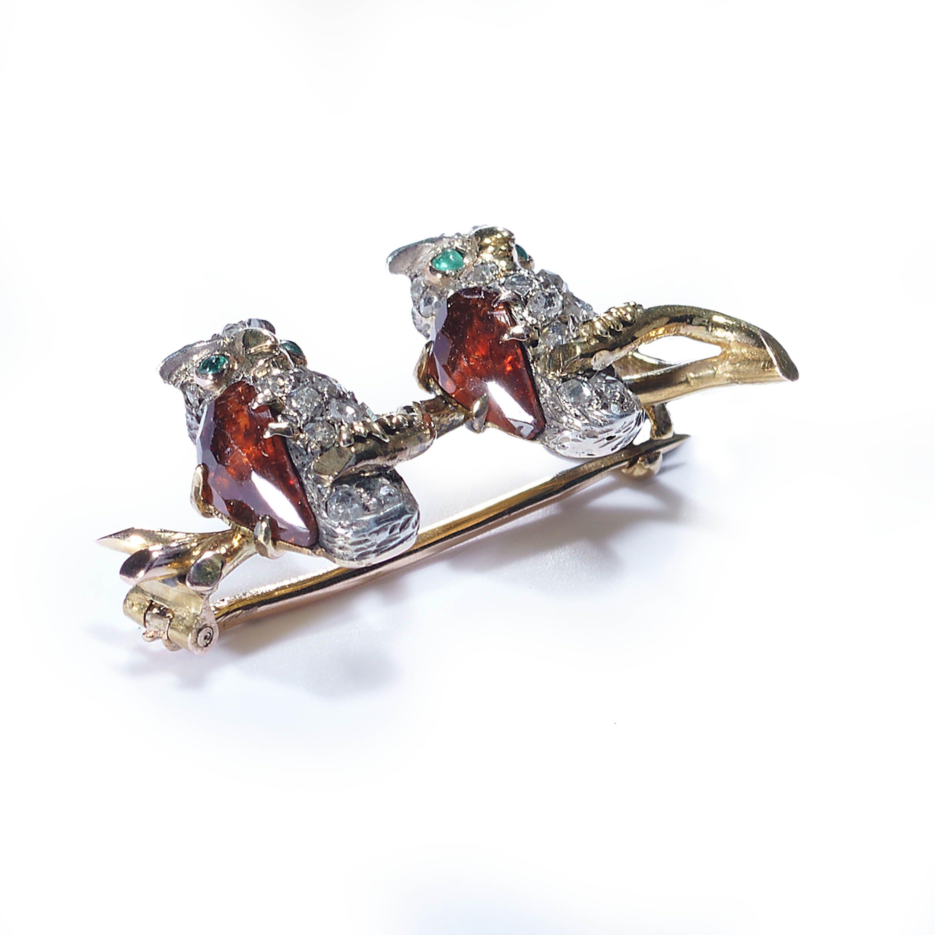 A French antique double owl brooch, with rose-cut diamonds pavé set, in silver, with the breasts represented by faceted hessonite garnets and the eyes set with cabochon-cut emeralds, with the owls sitting on a branch, mounted in gold, with a French
