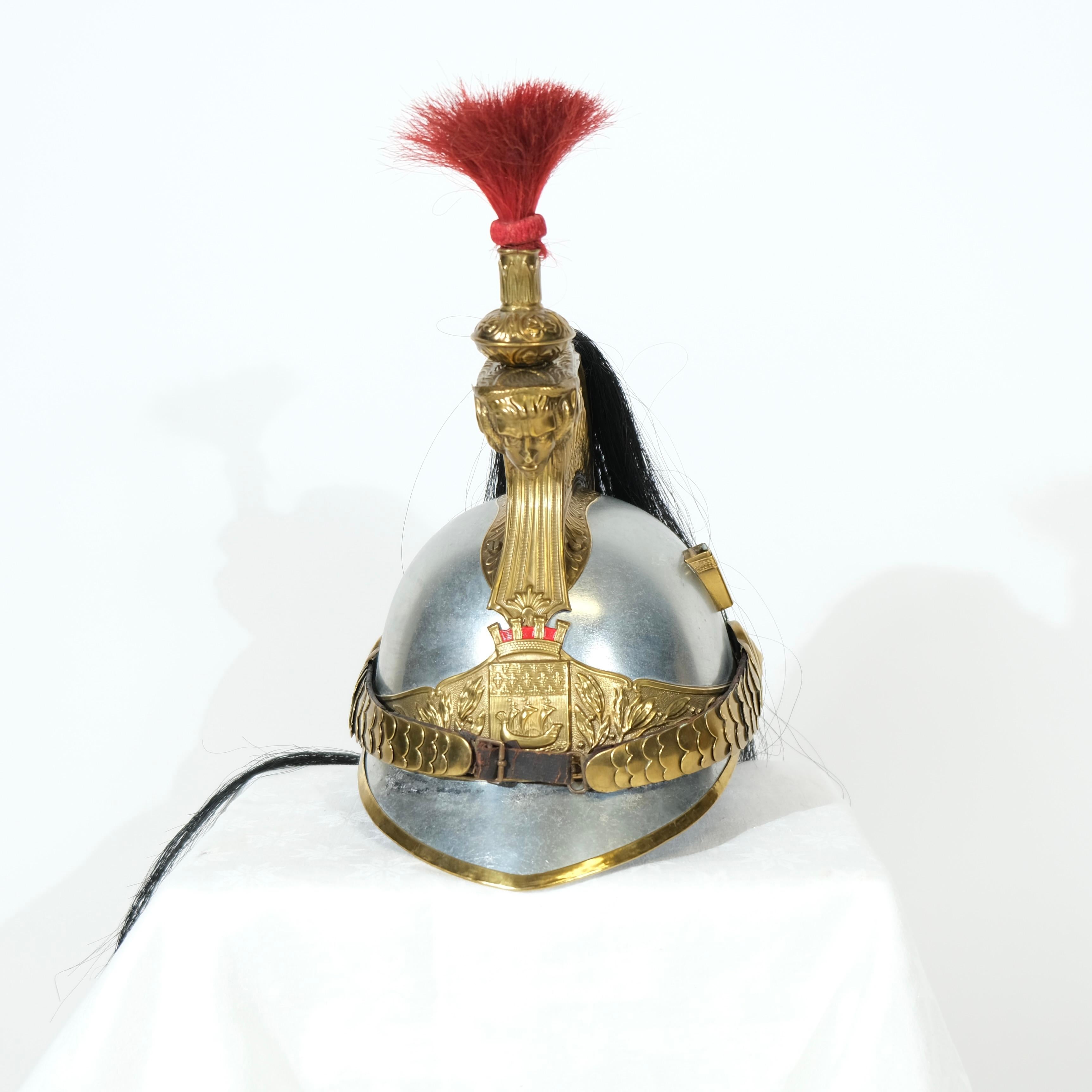 A French dragoon helmet, model of 1874. This type of helmet was typically worn by heavy cavalry, known as dragoons, in the late 19th century. The helmet features a brass crest with intricate decorative patterns, a plume of red horsehair, and a long