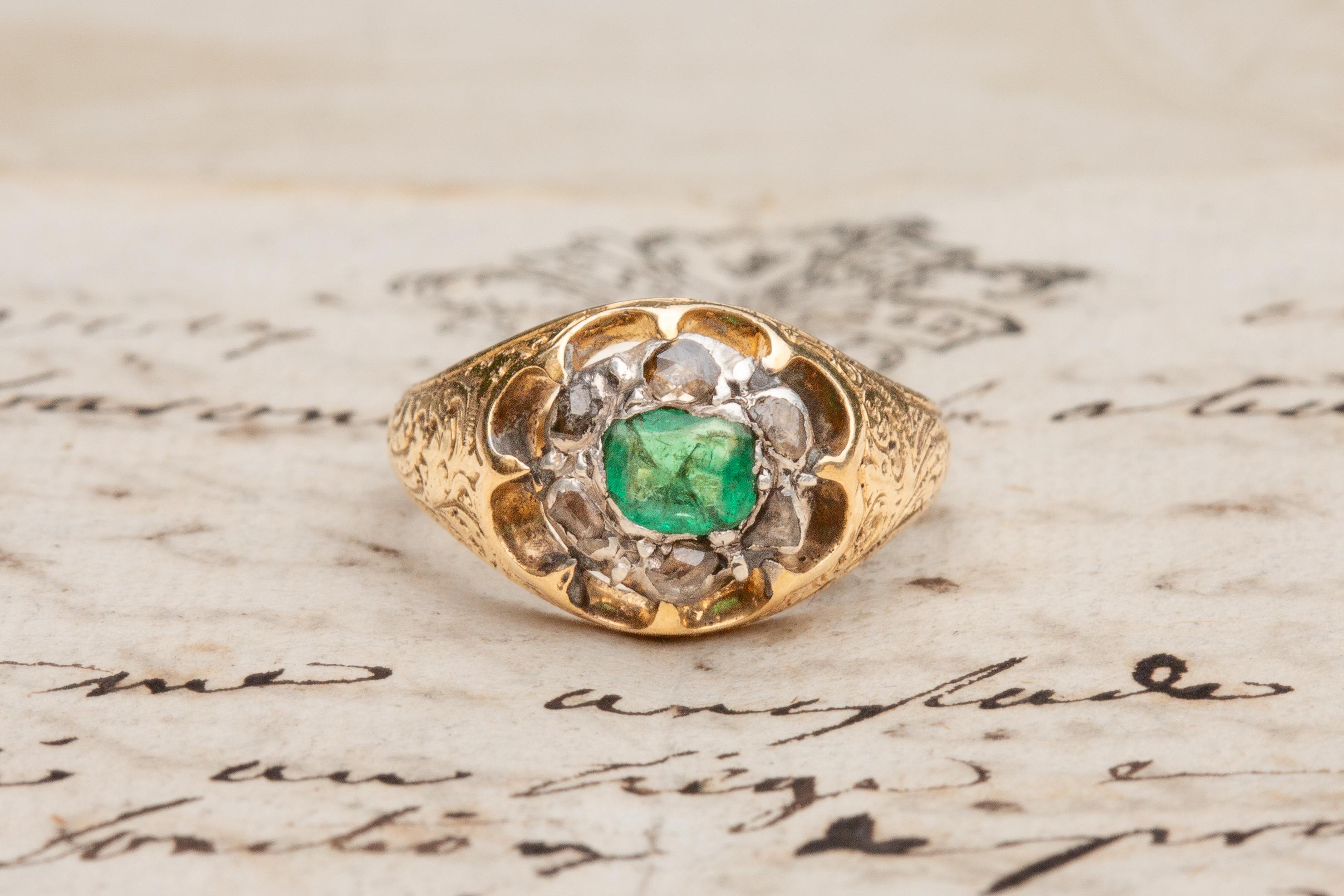 This unusual antique emerald and diamond ring was made in France and dates to the early 19th century.

In the centre rests a vibrant 0.3ct step cut emerald in an open-backed rubover silver setting. The stone is a wonderful vivid green colour and