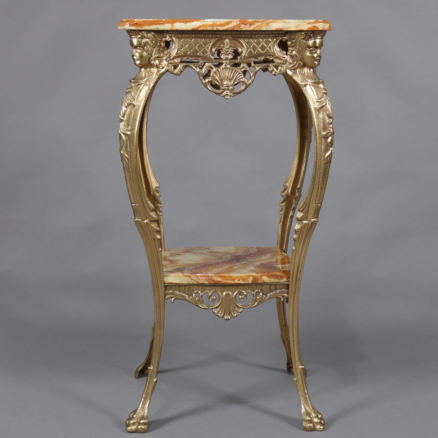 Antique French Egyptian Revival two-tiered plant stand features cast and gilt bronze frame with onyx top over pierced foliate and scroll apron, raised on cabriole legs surmounted by female masks and terminating in paw feet, lower onyx display shelf