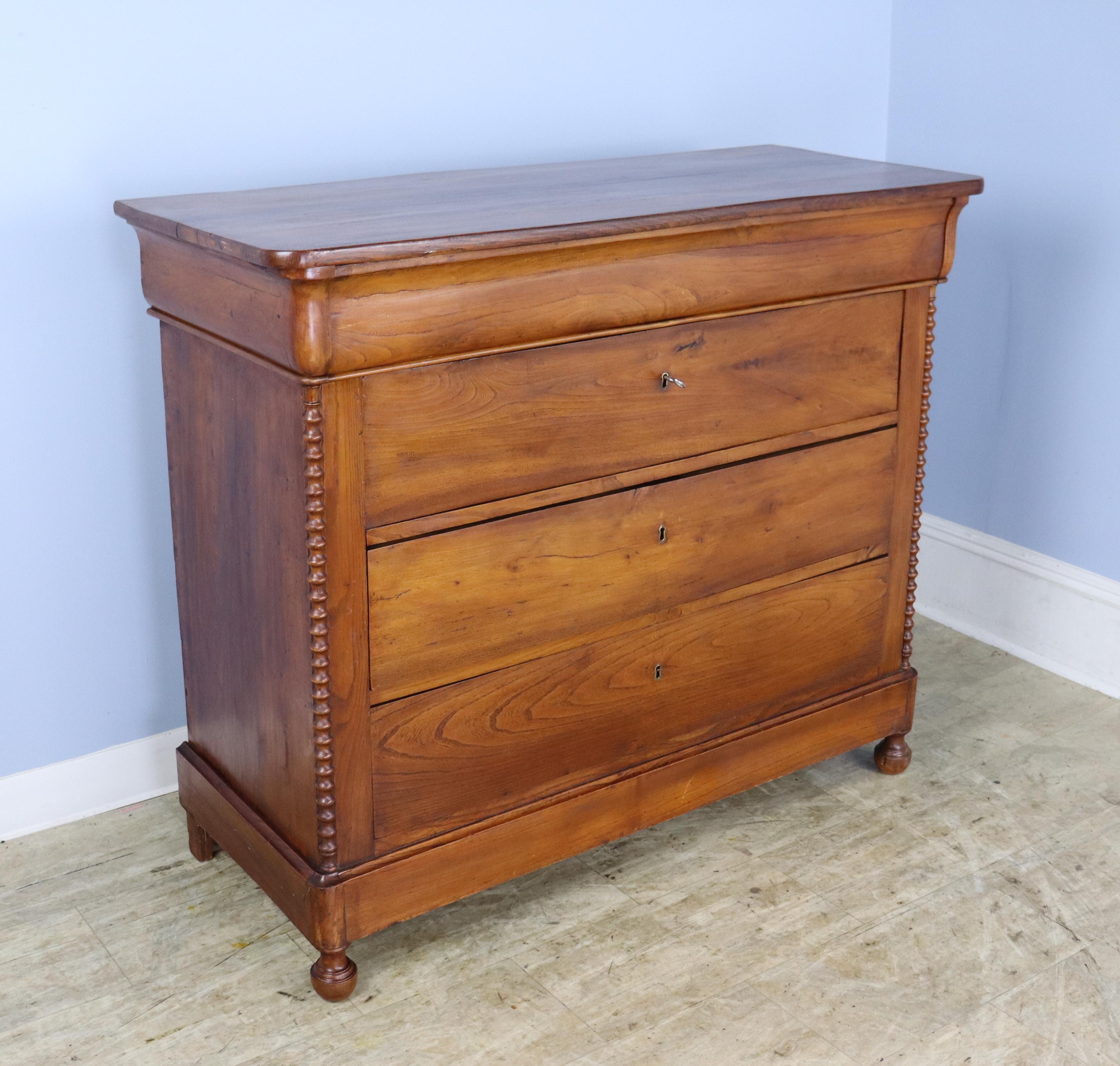 A fanciful French elm chest of drawers with turned columns at either side and sweet ball feet.  Classic Louis Philippe syle molded top drawer.  Single key pulls open all four drawers.  There is a slight warp to the third drawer which causes a small