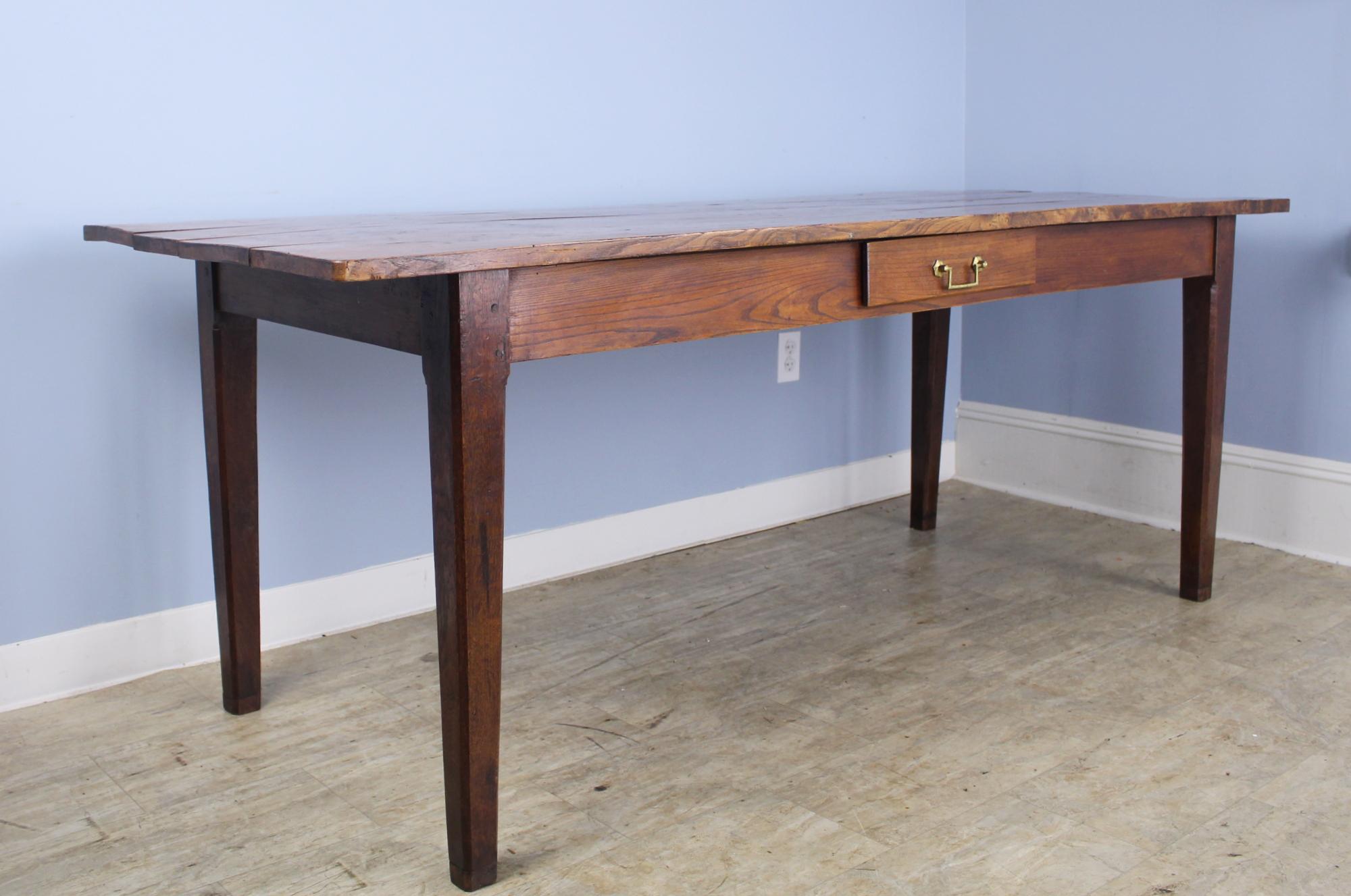 A handsome elm dining table or farm table with elegant tapered legs and a useful and decorative drawer. Handle has been replaced.
The top has lovely color, grain and patina. 24.5 inch apron height is good for knees and there are 61 inches between