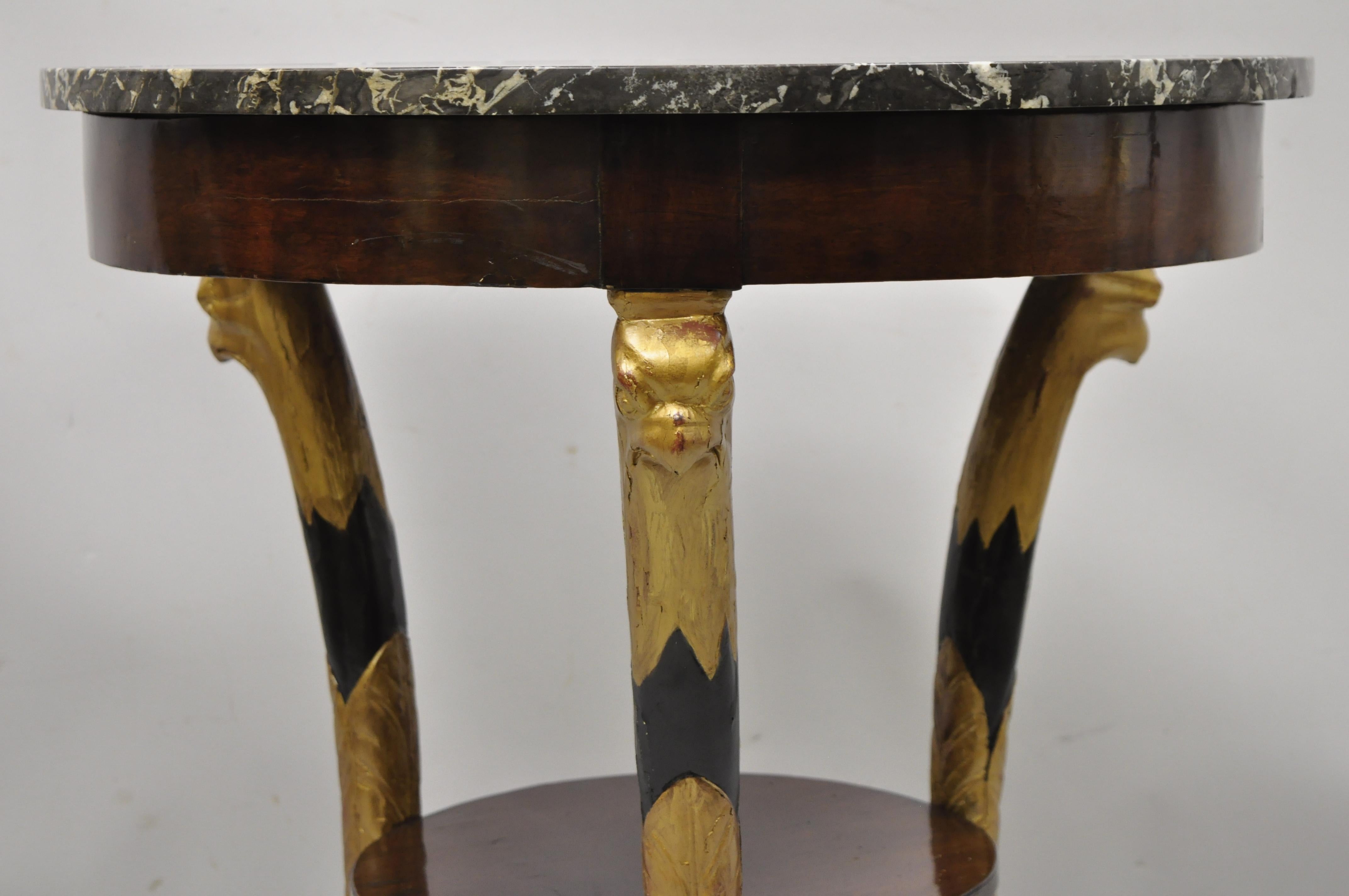 Antique French Empire Biedermeier round marble top gold gilt eagle carved gueridon center table. Item features round marble top with raised edge, gold gilt eagle heads, lower shelf, ebonized finish, paw feet, beautiful wood grain, very nice antique