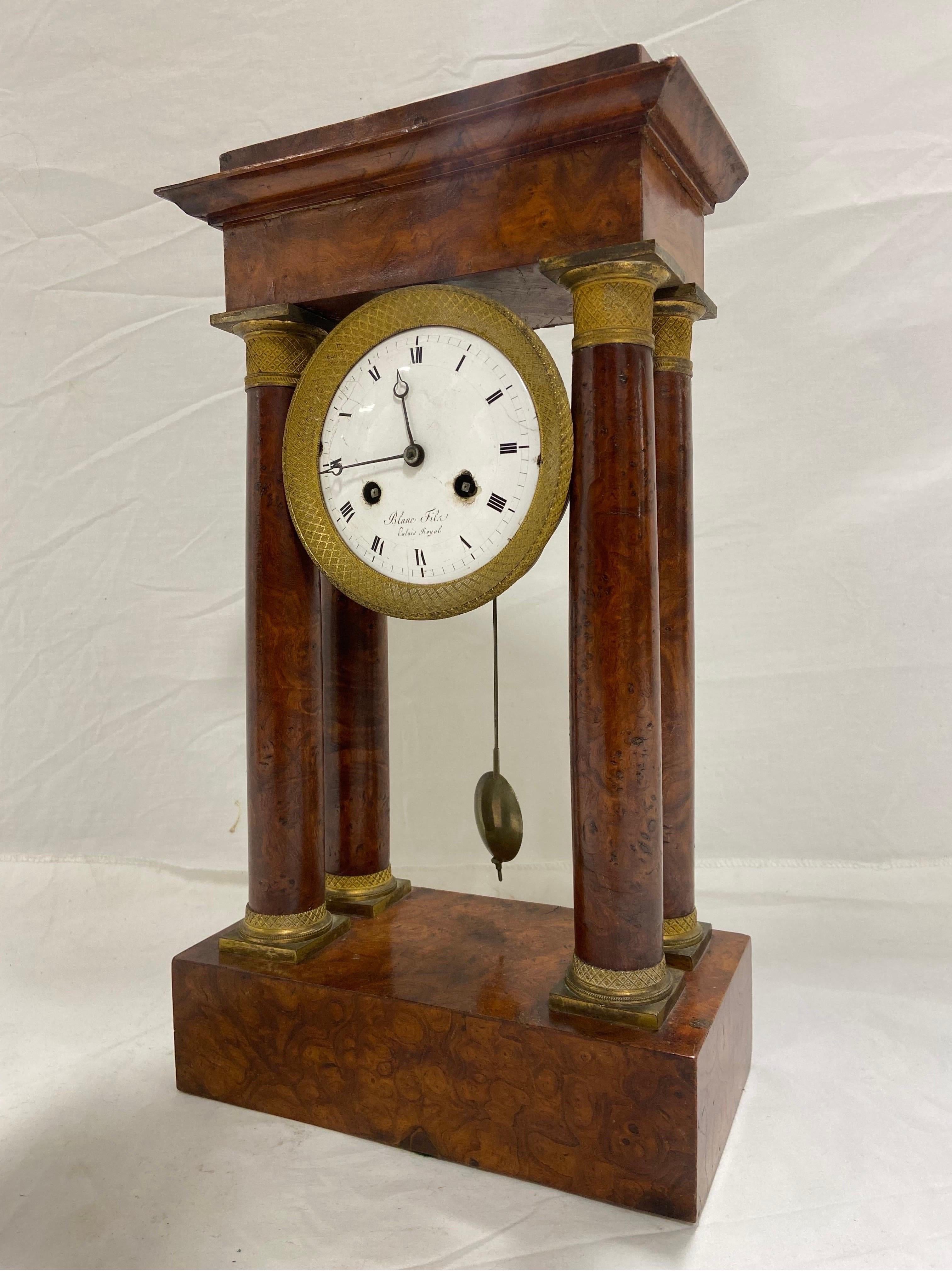 A French Empire style antique ormolu mounted portico table clock. The mid 19th Century architectural case has four columns. The white enameled Roman dial is signed Blanc Fils Palais Royale and housed within a circular drum case containing the