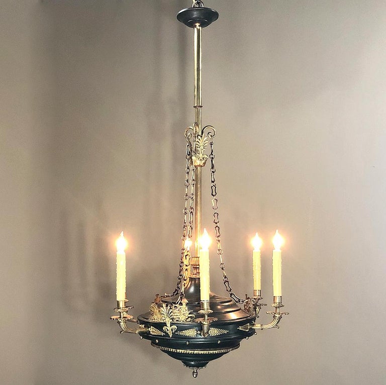 Antique French Empire bronze and brass chandelier is a marvel of craftsmanship! Dark green painted body is festooned with polished bronze adornment, with styles influenced by Napoleon's Egyptian campaign. A Roman maiden (goddess?) rides a chariot