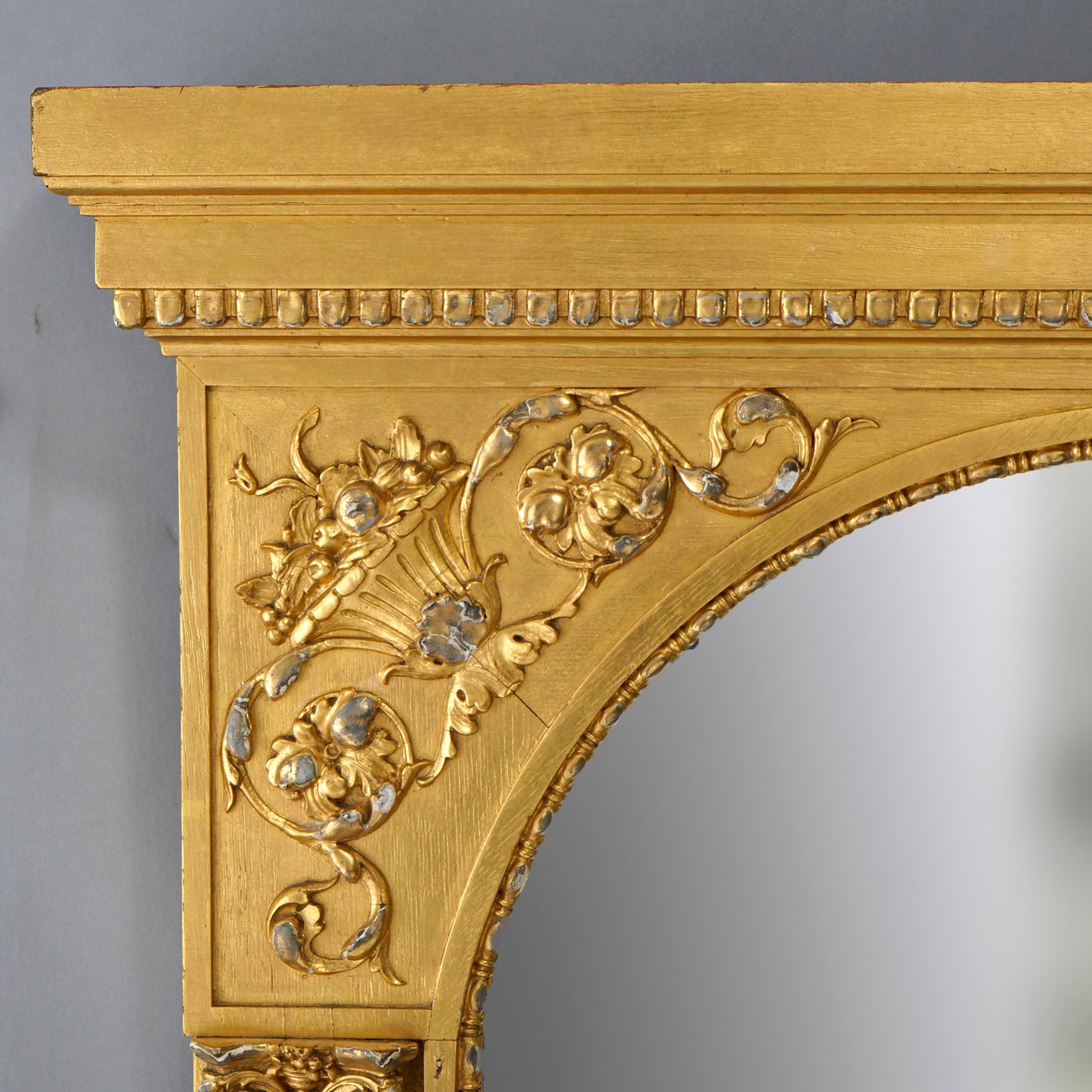 An antique French Empire classical style wall mirror offers giltwood construction with frame crest having floral, foliate and panier de fleur elements over arched mirror with flanking Greco reeded column supports, 19th century

Measures- 29.75'' H x