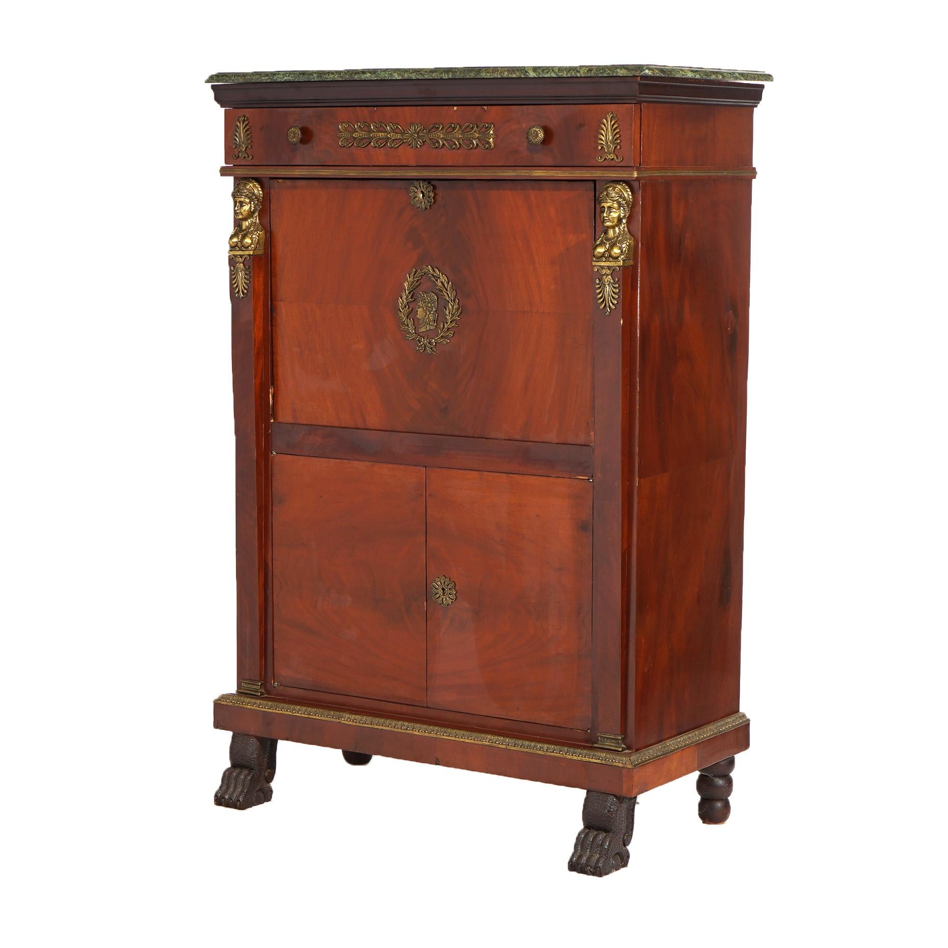 An antique French Empire abattant secretary offers flame mahogany construction with upper drawer over drop front desk opening to interior with pigeon holes and drawers, surmounting lower double blind door cabinet; cast ormolu mounts throughout