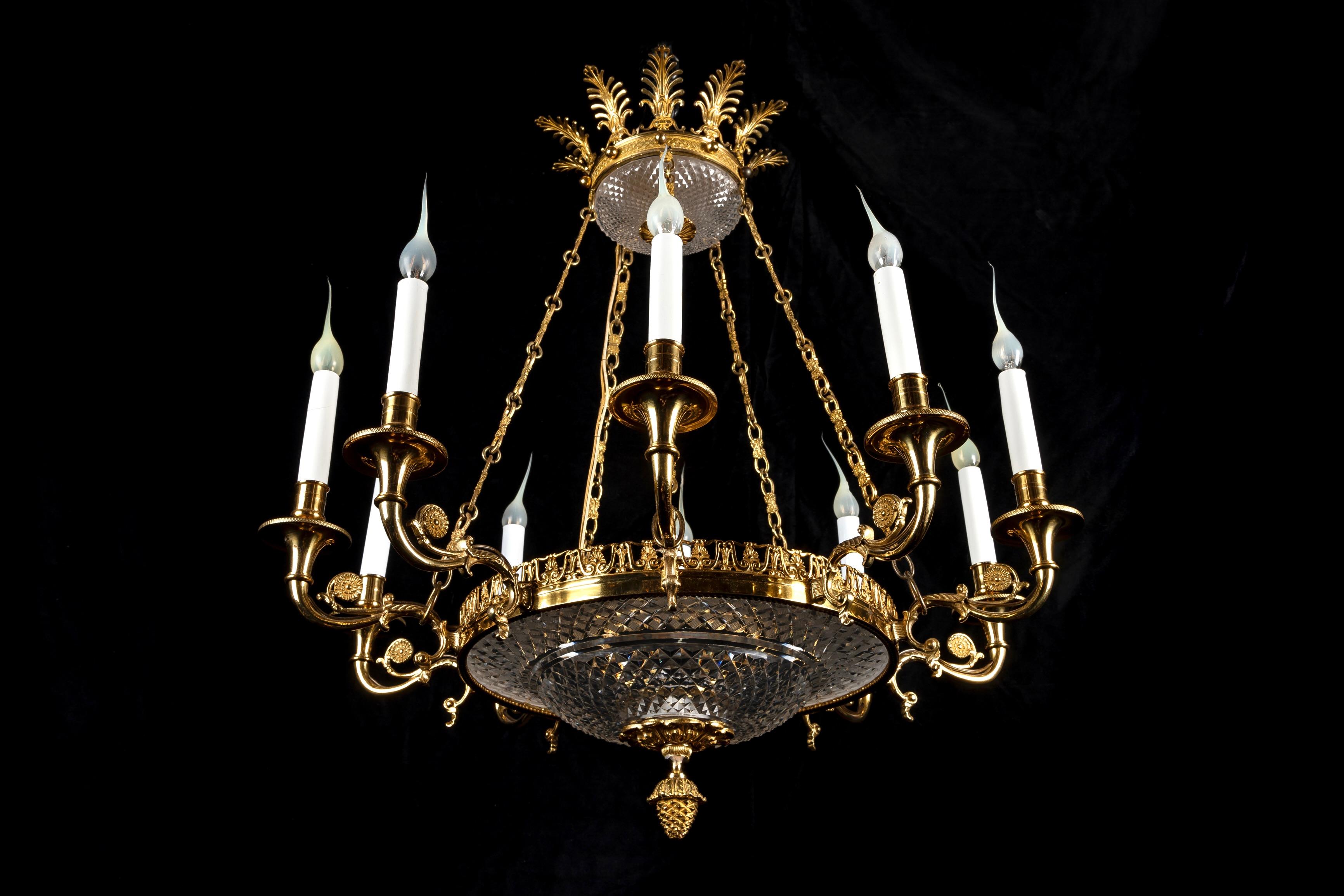 Ce lustre néoclassique Empire français ancien est fabriqué en bronze doré et en cristal taillé. Il présente un cadre circulaire orné de motifs classiques. Le lustre est suspendu par une série de chaînes en bronze doré reliées à une partie supérieure