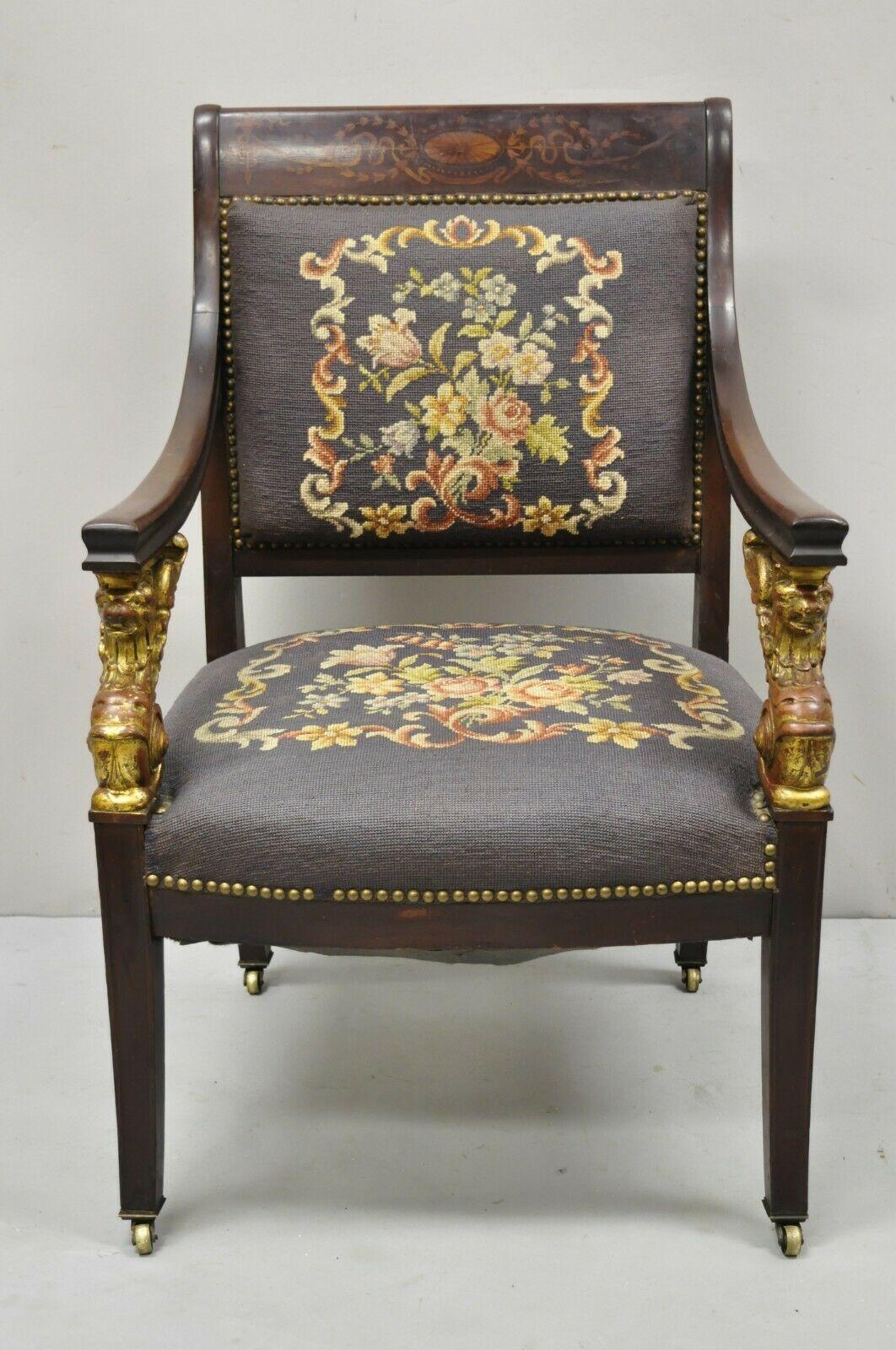 Antique French Empire giltwood winged Griffin needlepoint and inlay parlor arm chair. Item features gold gilt wood winged griffin arm supports, bell flower, pinwheel, and ribbon inlay, brass rolling casters, floral needlepoint back and seat, very