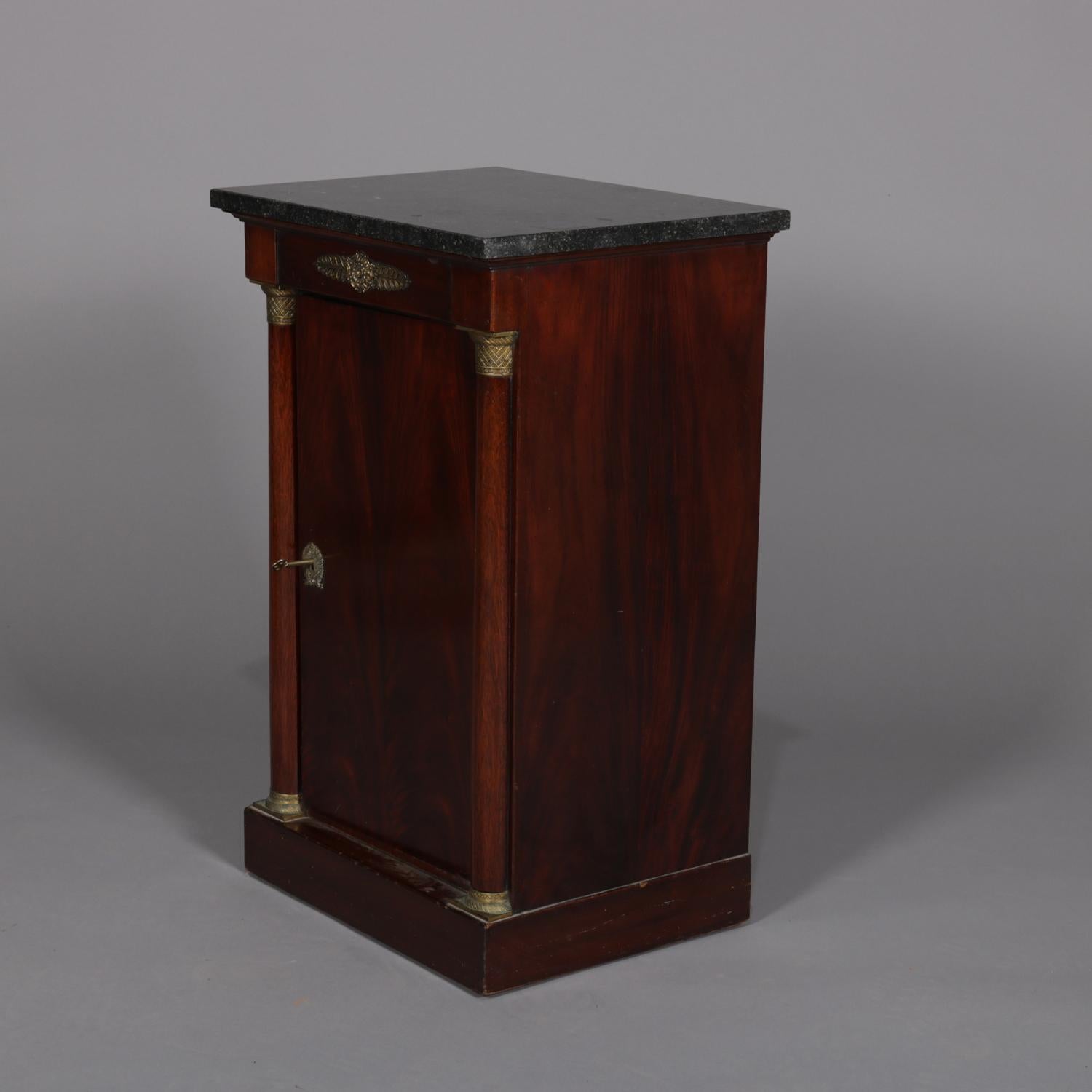 An antique French Empire side cabinet features marble top surmounting single door mahogany case having flanking Corinthian column supports, cast bronze attachments throughout, locking and with key, case interior open and without shelving, circa