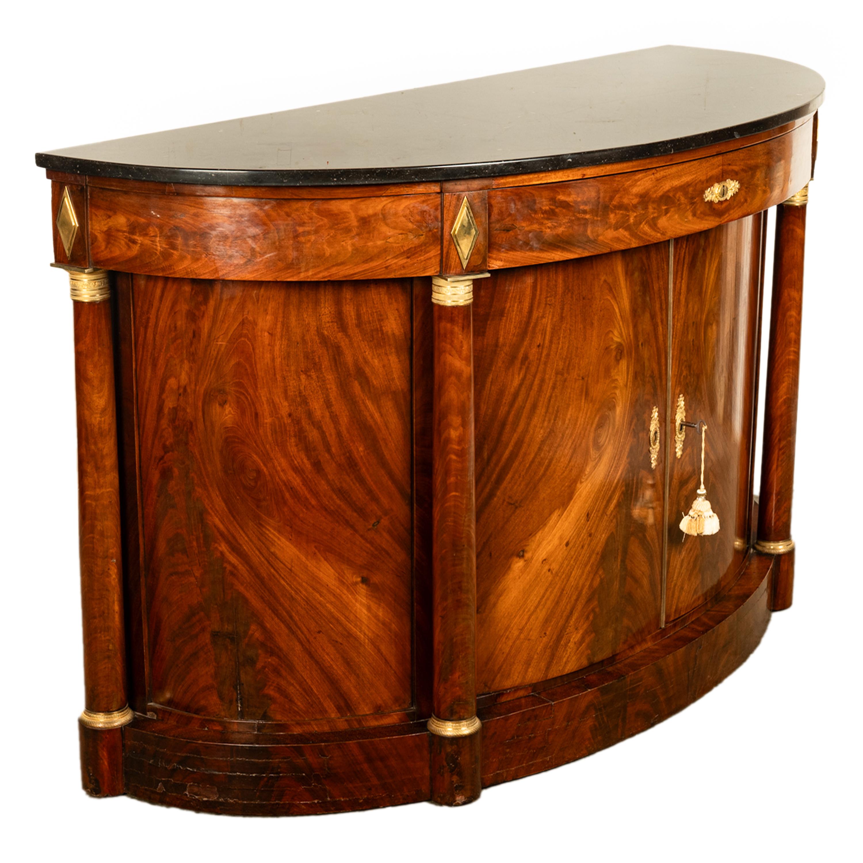 Un bon cabinet de demi-lune Empire français en acajou flammé, avec dessus en marbre et monture en bronze doré, vers 1810.
Le meuble est doté d'un plateau d'origine en marbre noir tacheté, la base en demi-lune est équipée d'un seul tiroir avec un