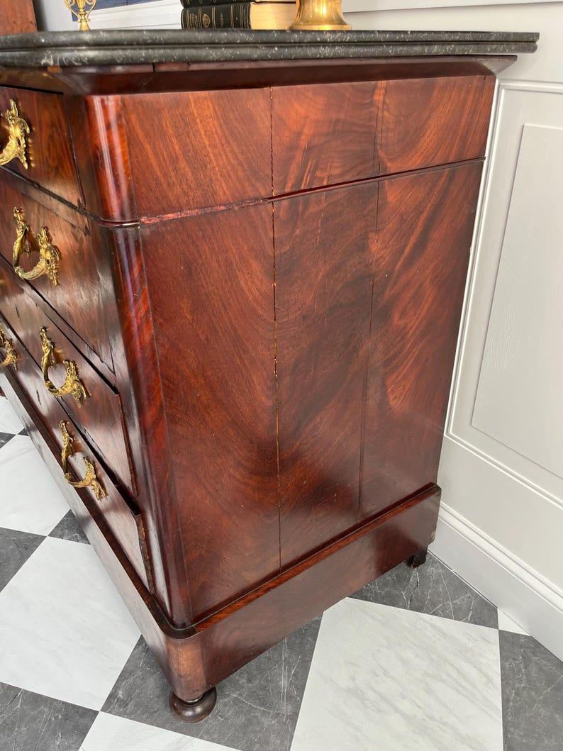 A showstopping antique French Empire-style chest of drawers with a rich, storied past — and ready for its next chapter in a thoughtfully styled home.

Dating to the mid-1800s, this dramatic five-drawer dresser features stunning bookmatched mahogany
