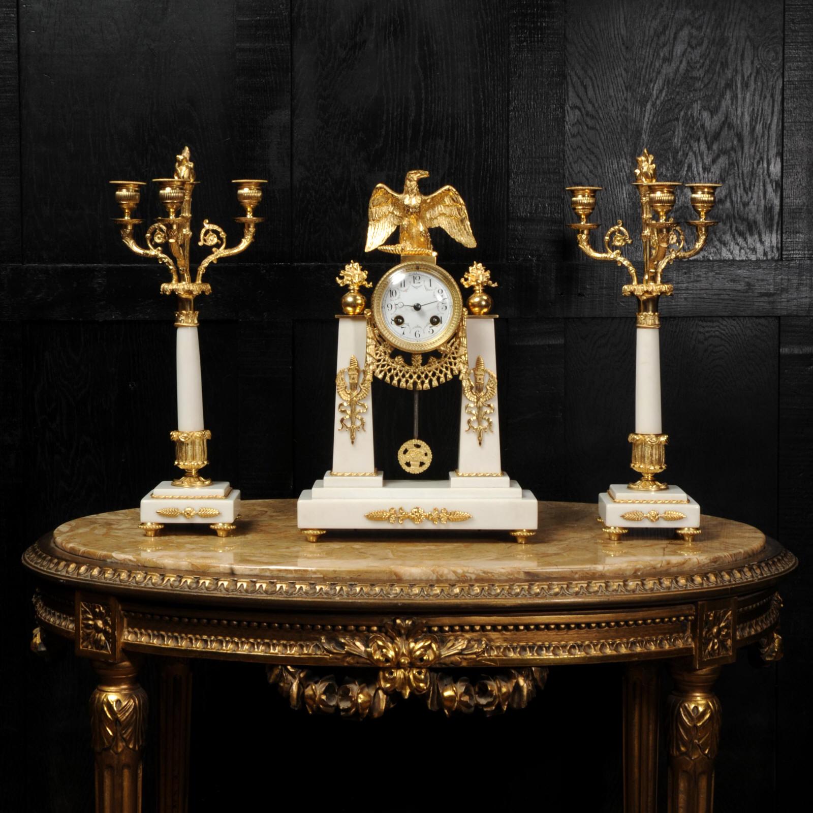 A stunning original antique French clock set circa 1890. It is of Empire design in crisp white Carrera marble and ormolu (finely gilded bronze). To the top is a beautifully modelled spread eagle with flaming finals to the sides. The clock is