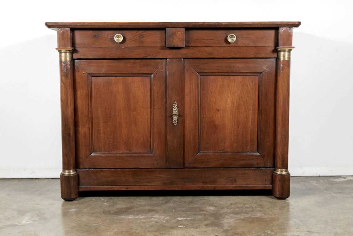 Early 19th century French period Empire buffet handcrafted of oak near Mont Saint-Michel, an island commune in Normandy, having two drawers over two doors flanked by support columns with original gilt-bronze capitals. Each column ending in