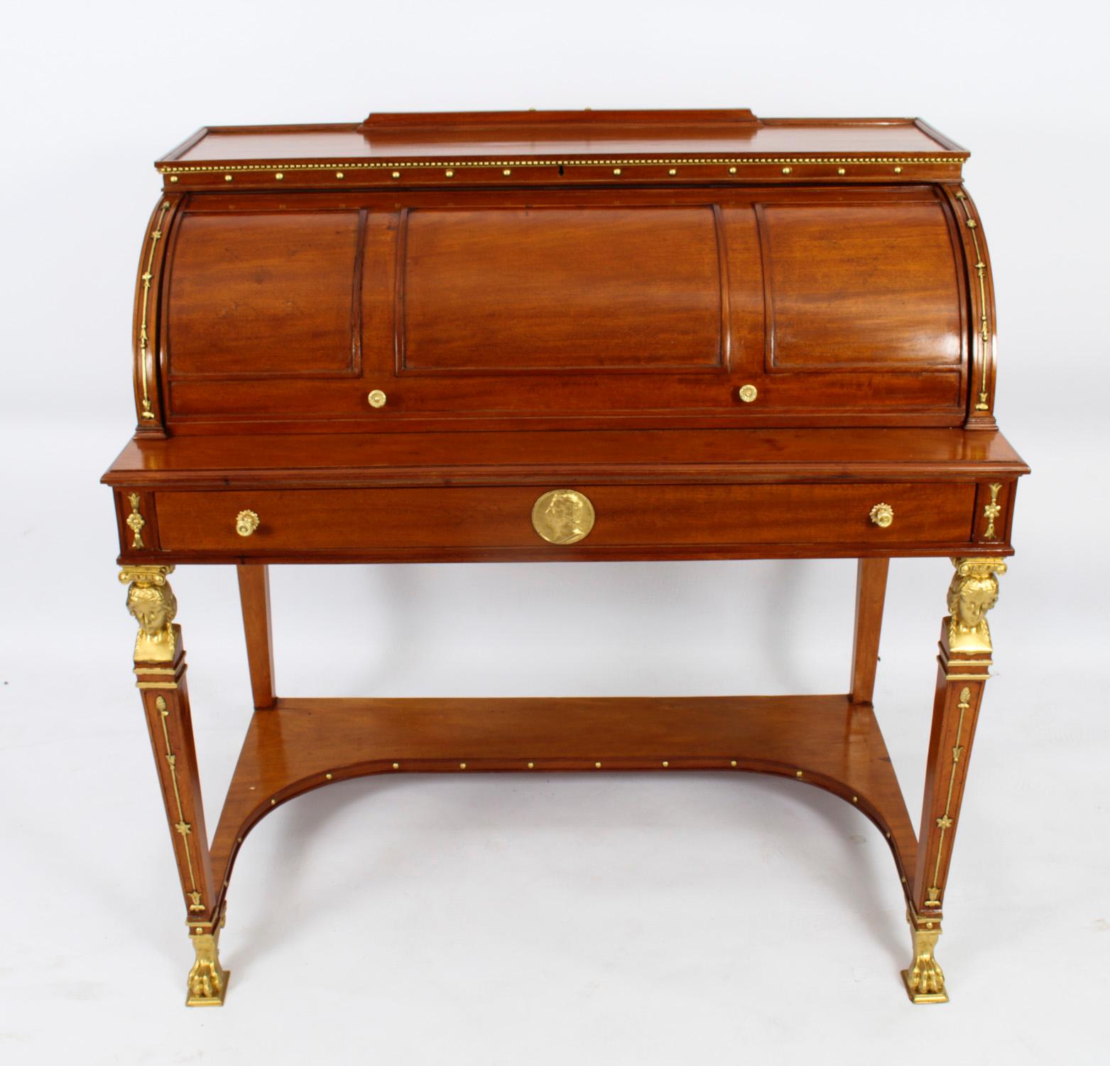 An Empire Revival mahogany and parcel gilt cylinder bureau, Circa 1880 in date.

The panelled roll top enclosing a green inset leather writing surface and an arrangement of drawers and pigeon holes, above single frieze drawer.

It is stands on