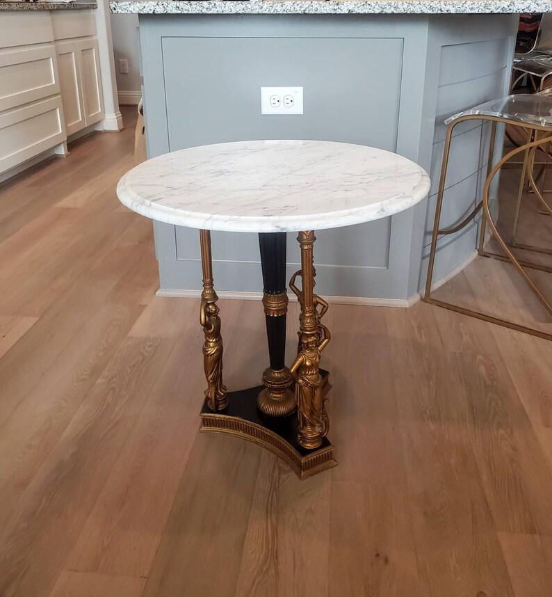 A rare and magnificent antique French guéridon, finished in classic Empire Revival taste, having a circular white with gray veining marble top, elegantly rising on a metal tripartite base with three gilt bronze toned female figural supports and a