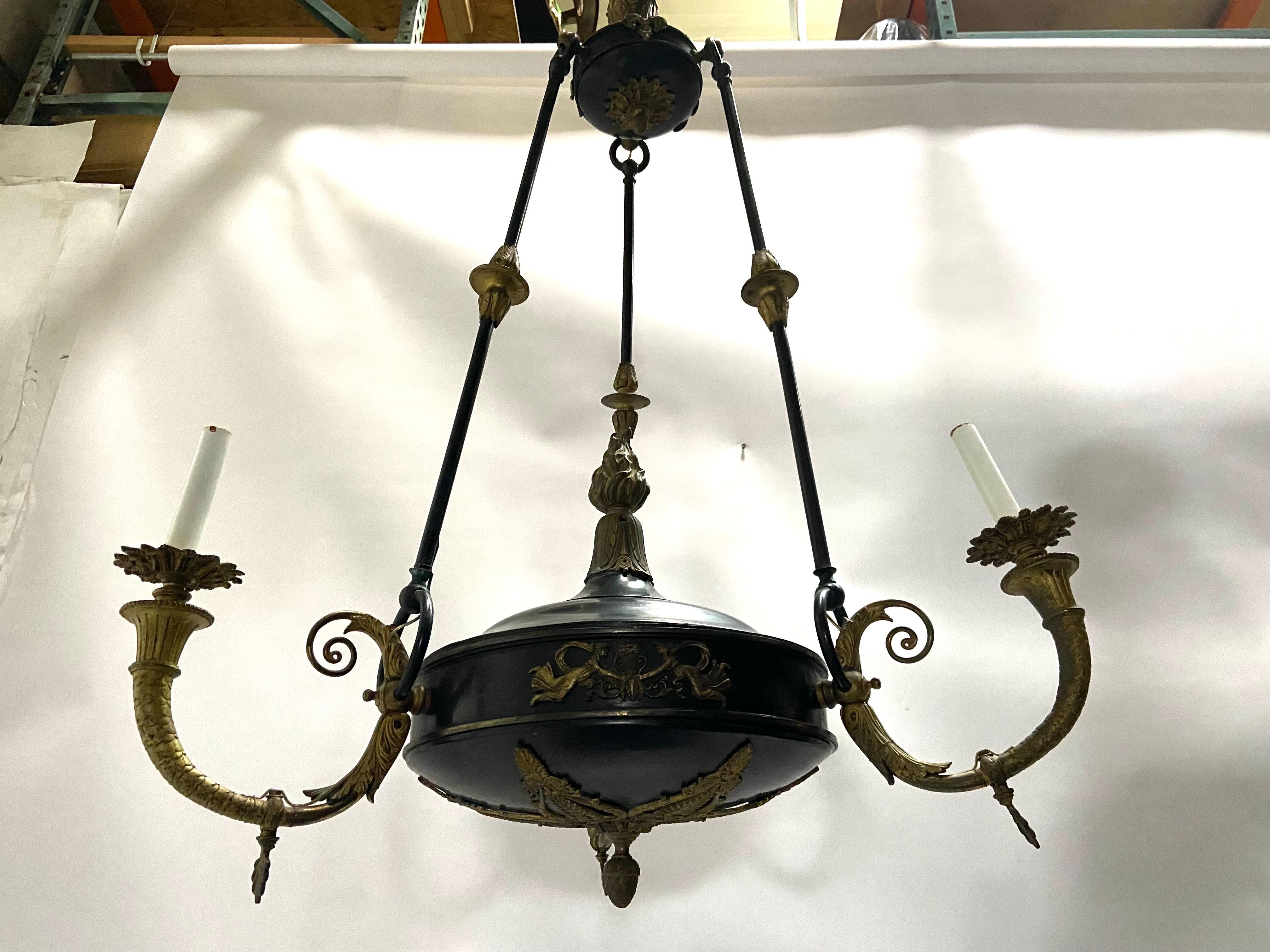 An antique, circa 1900 - 1920, French Empire style bronze three light chandelier. The underside of the chandelier features a highly detailed stylized acanthus leaf pierced ornament with a drop down acorn ornament. Each of the three arms features a