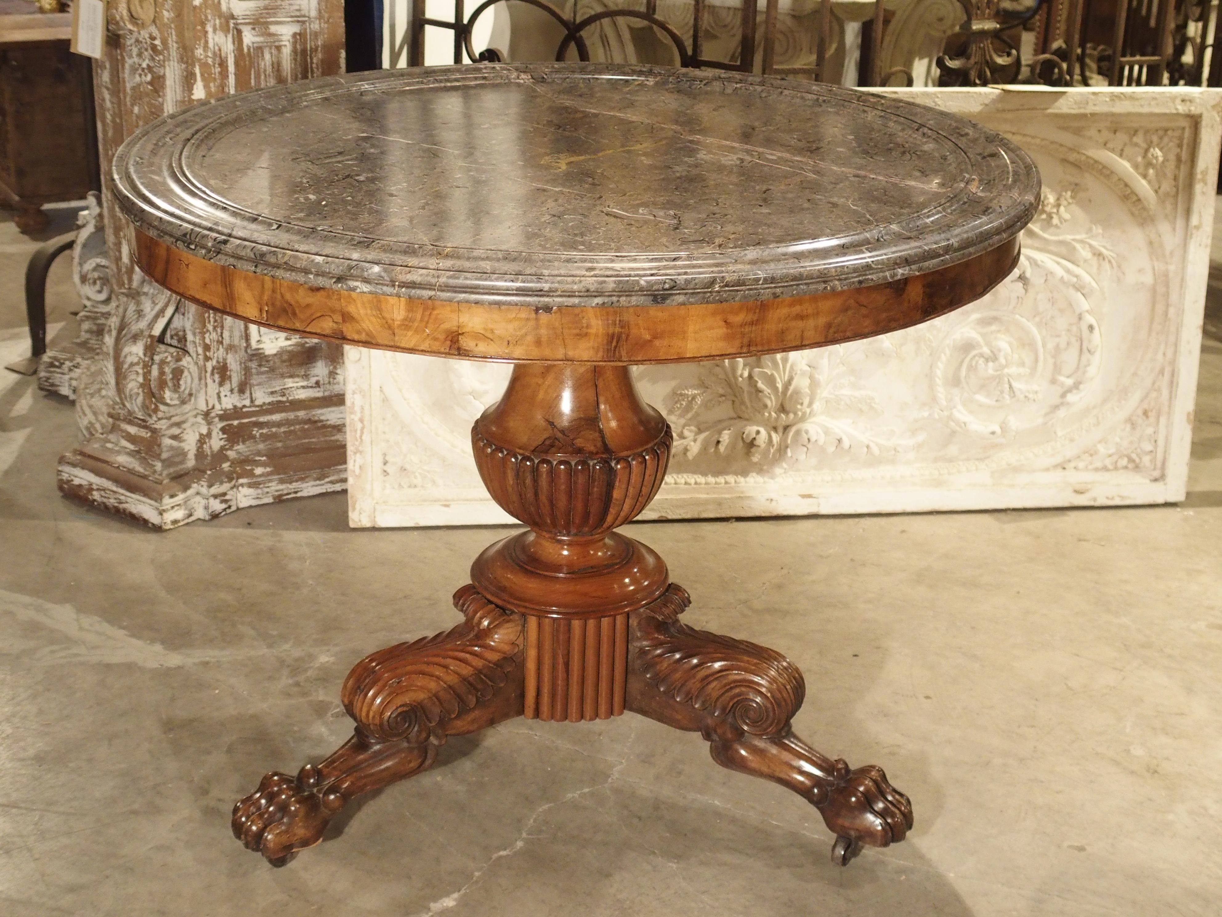 From France, this beautifully designed round mahogany table is in the French Empire style. It has a grey and white veined marble top with grooved moldings at the periphery. Just beneath the stone, is an unadorned, burled mahogany veneer. The central