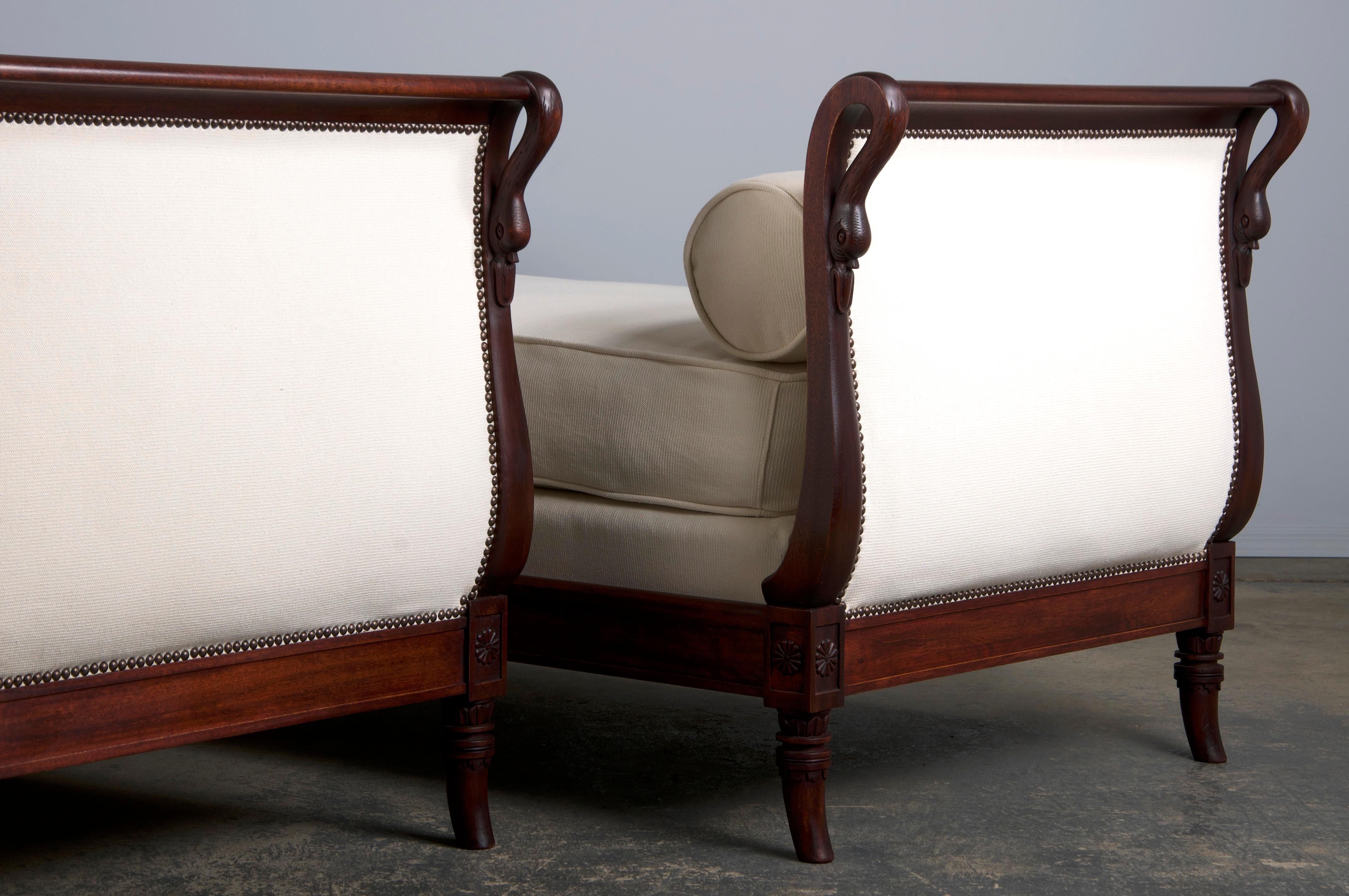 An exquisite pair of early 19th-century French Empire daybeds, sourced directly from Paris, France. Masterfully crafted from solid mahogany, these daybeds feature sleigh-shaped frames adorned with elegantly hand-carved swan-neck corners. The pair