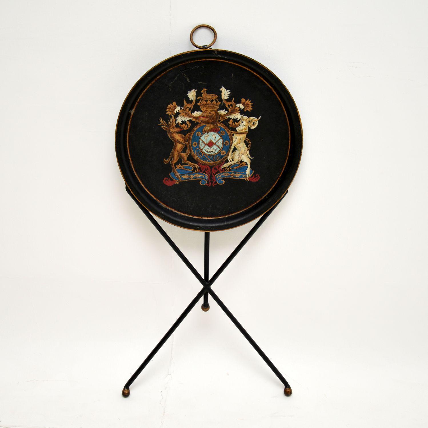 A lovely antique folding side table in enamelled metal, otherwise known as tole. This was made in France, it dates from the 1900-1920’s period.

It is very well made, and decorated with a beautiful coat of arms. There is a ring handle on one side,