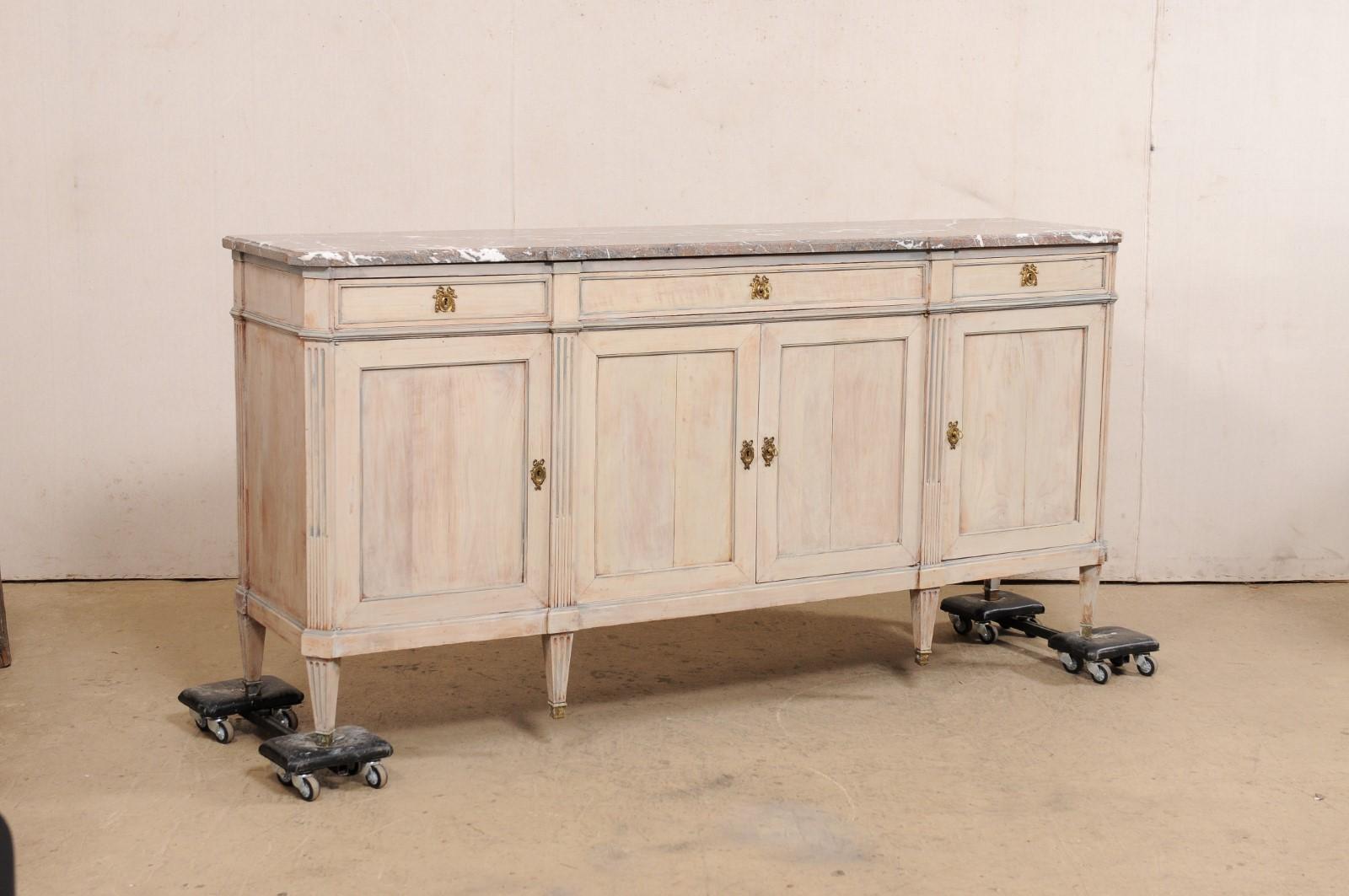 A French wooden sideboard, with flute-carved accents and original marble top, from the late 19th to early 20th century. This antique buffet console from France has a marble top with canted front corners and a pair of outward notched accents at front