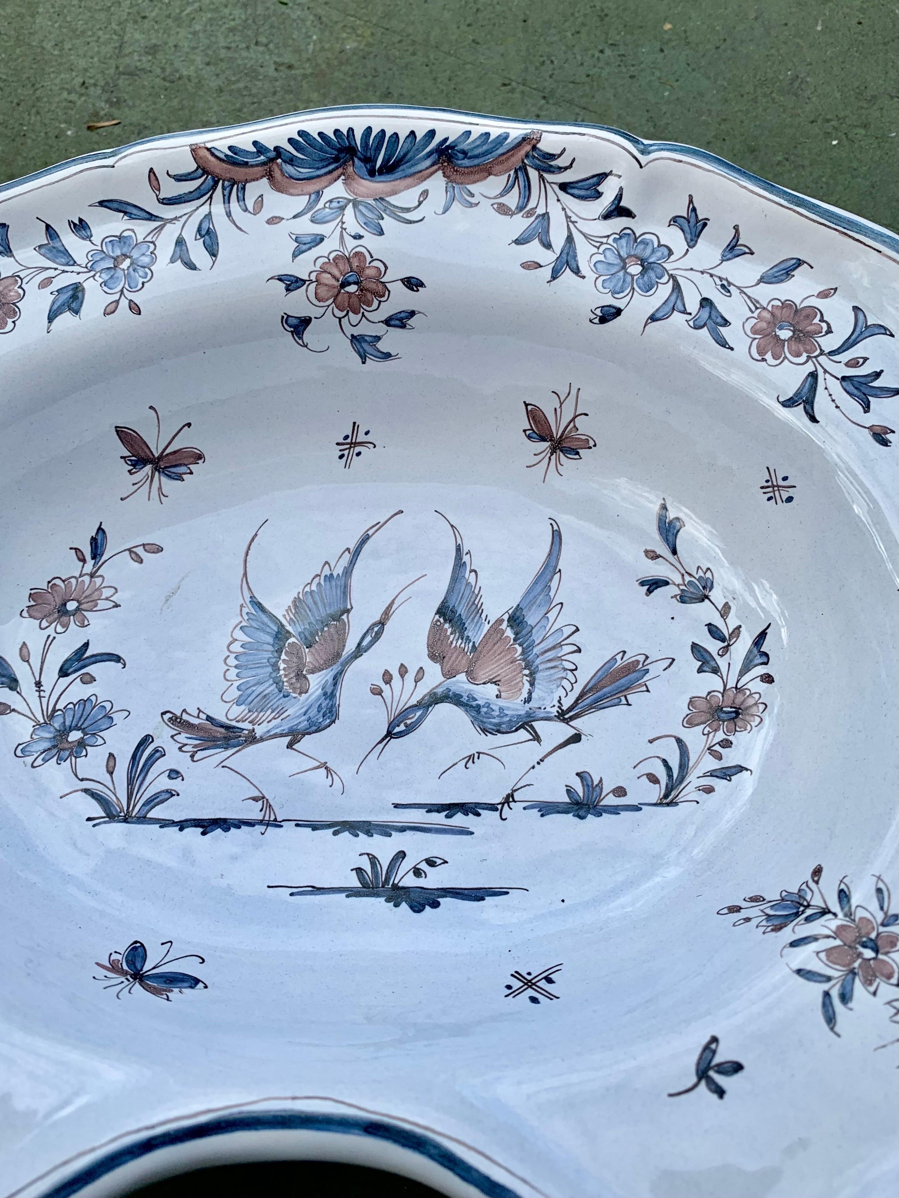 An antique French faience men's shaving bowl, having lovely and delicately hand painted birds and flowers. Signed en verso and with copper wire for wall hanging.
  