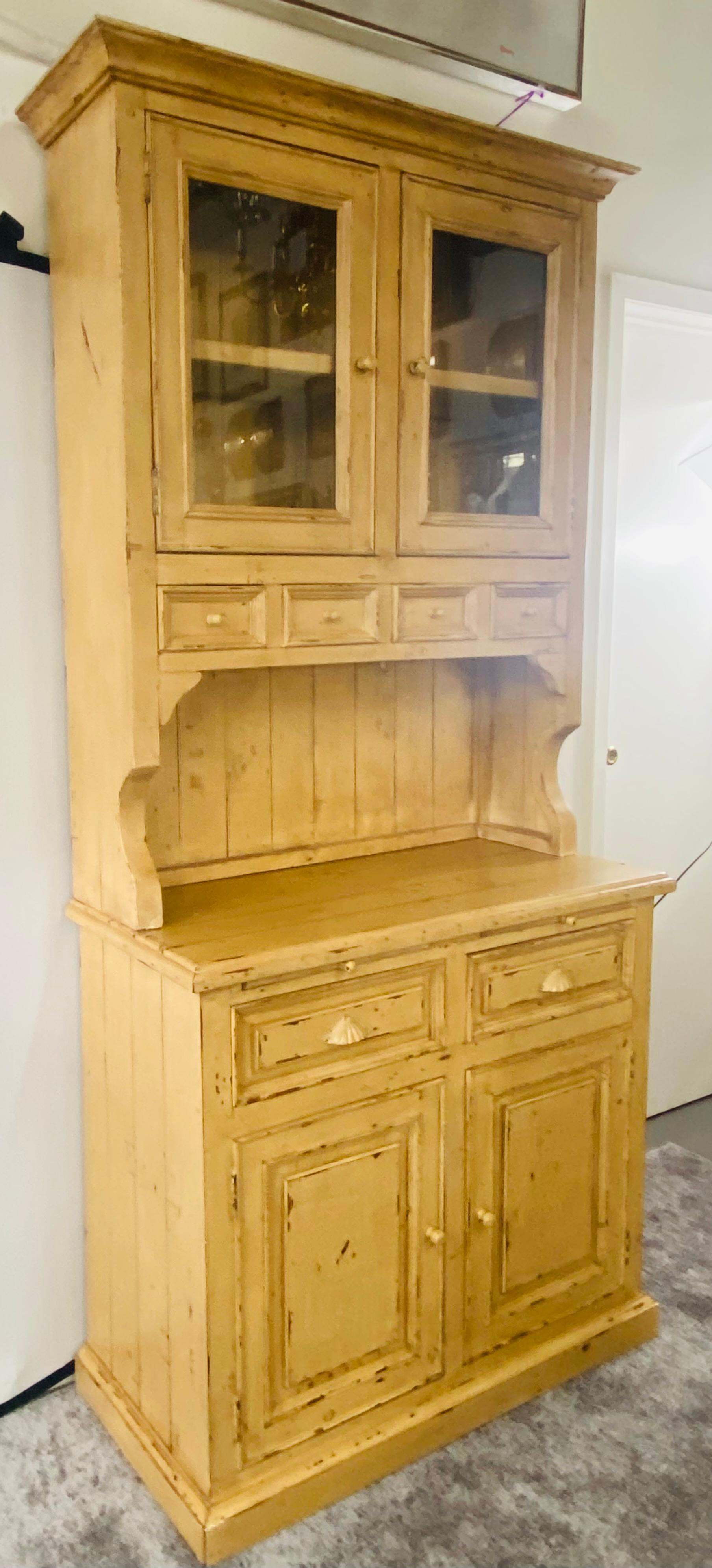 A stylish and timeless antique off-white/ beige French farm style cabinet with hutch in distressed look. The cabinet comes in two pieces. The upper piece features two glass door with shelves and four small drawers with dovetails joints. The bottom
