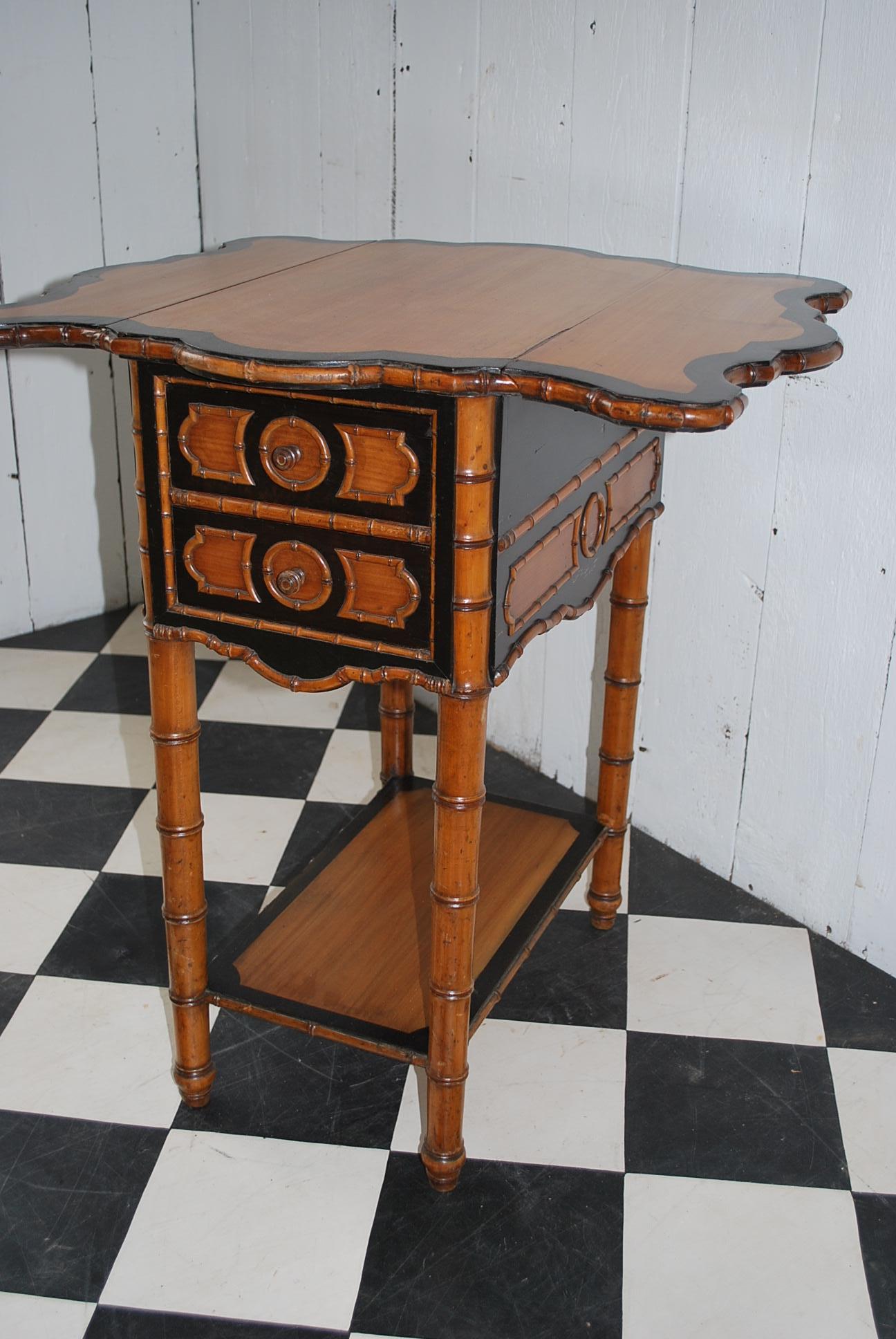 This is a good quality French antique faux bamboo occasional table with contrasting ebonized banding against a figured satin birch background. An unusual example of its kind with two small drawers to front and a drop down cupboard to rear. Standing