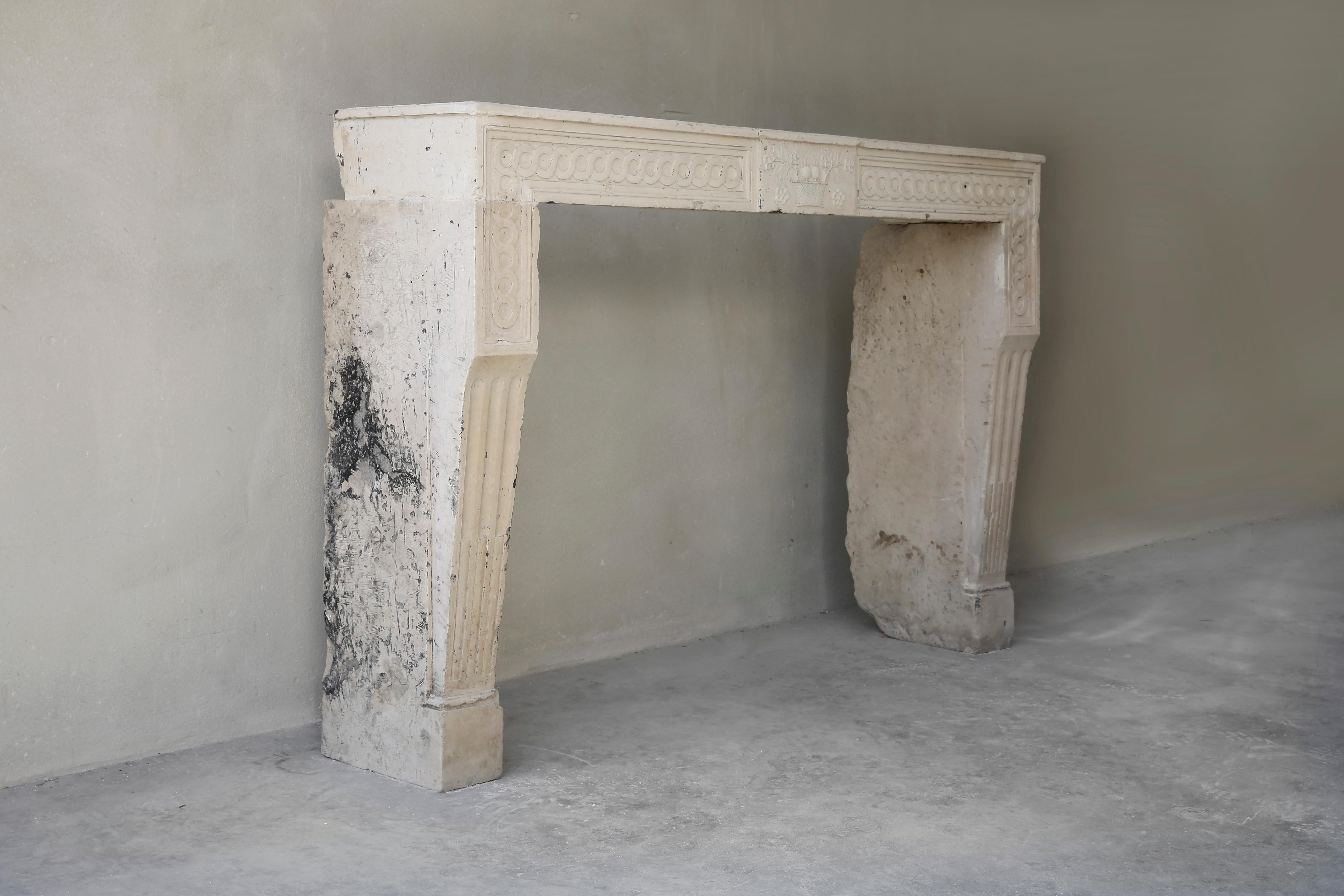 Beautiful carved antique French limestone mantel fireplace. The chimney is in Louis XVI style and dates back to the 19th century. In the front there is a beautiful ornament and also the legs are decorated with cannel lures. The decorations in the
