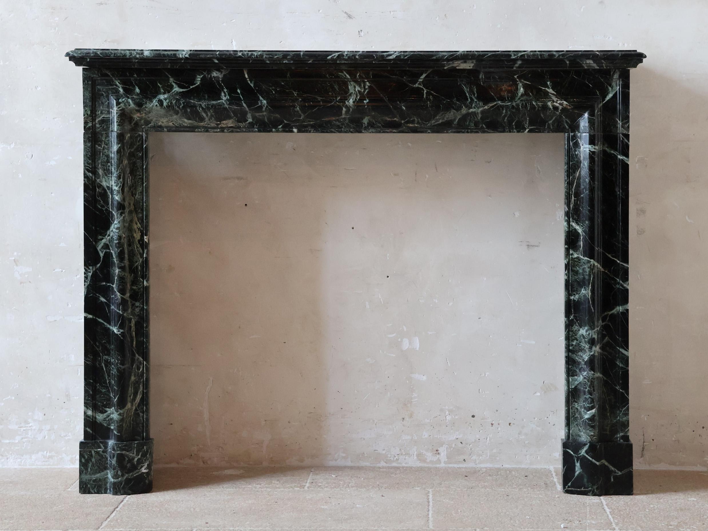 This refined antique marble fireplace is crafted from deep green marble that appears almost black, featuring delicate veining in white and light green tones. The minimalist yet solid design, with a straight marble mantel and squared legs, makes it a
