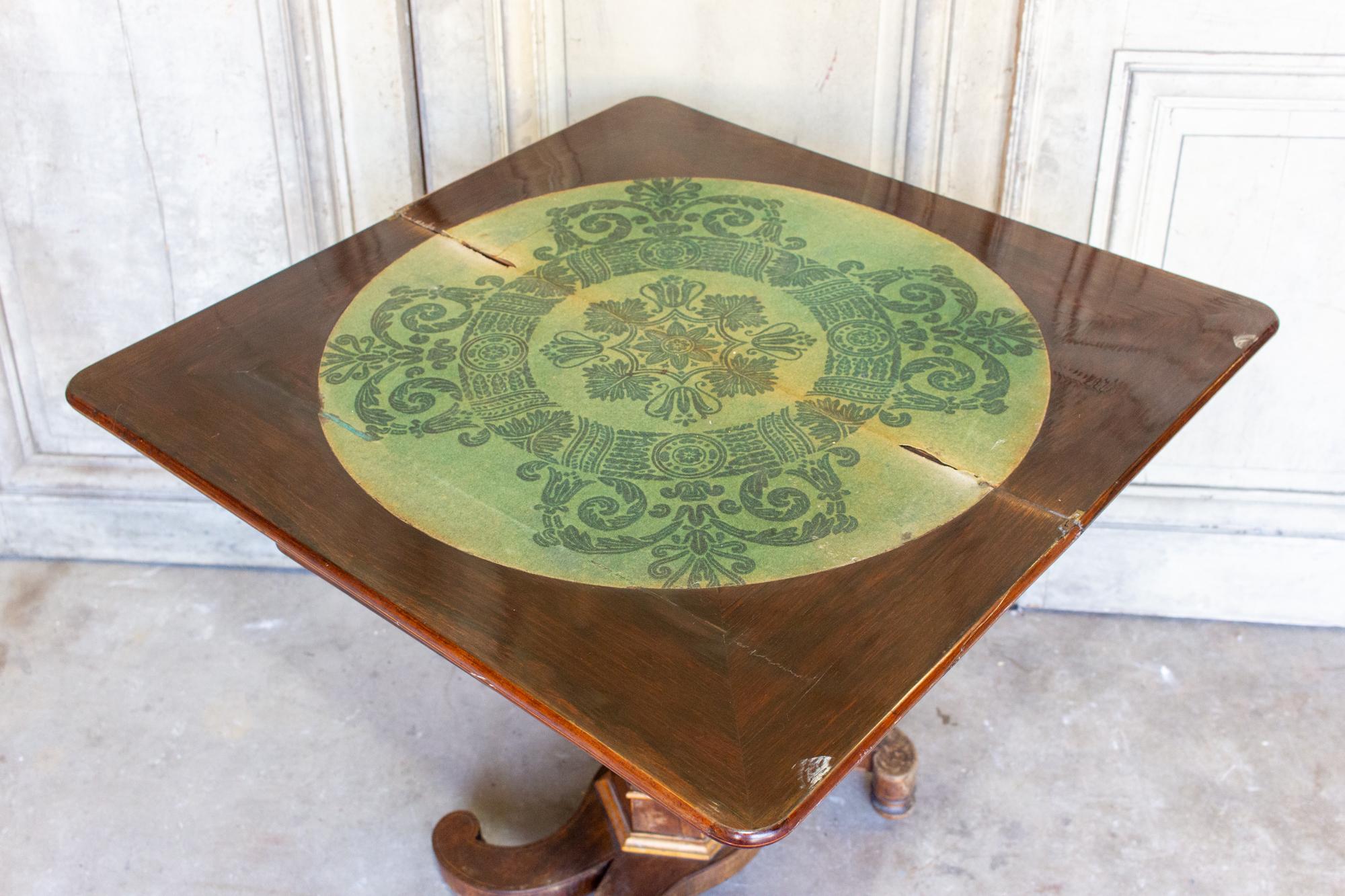 This antique French folding game table and console features inlaid wood details in the top and front. The central pedestal base has four curved legs. The inlaid veneer decoration is delicate scrollwork, appearing on both the top of the piece and the