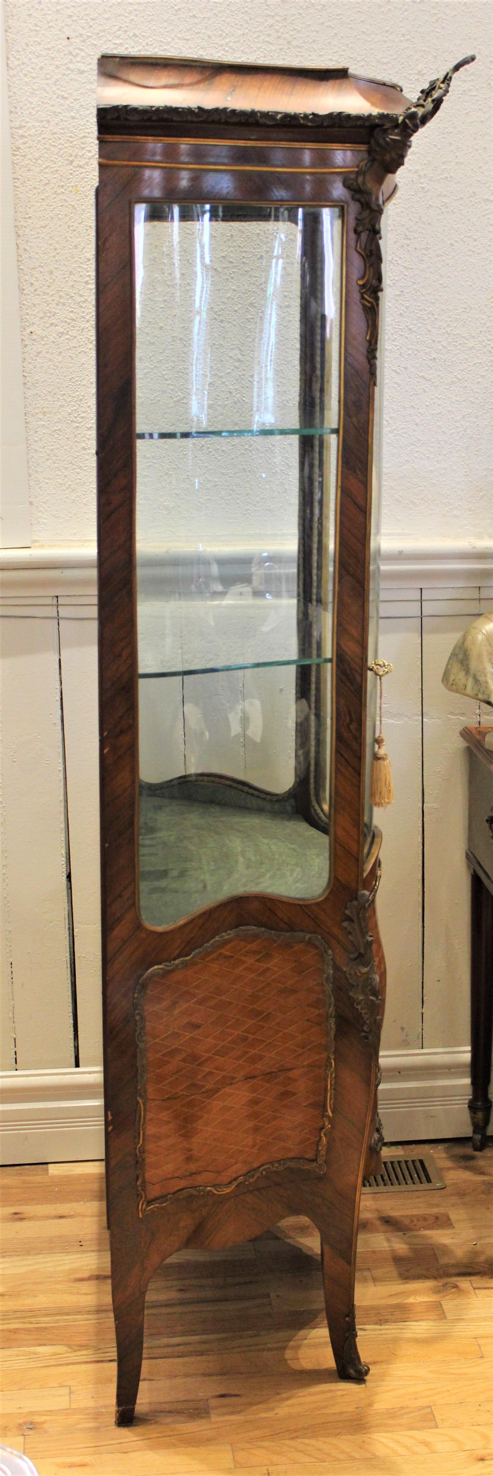 Ce meuble vitrine français du 19ème siècle est de style Louis XV à une porte, en noyer, de forme Bombay. La vitrine est décorée de montures figuratives détaillées et élaborées en bronze doré moulé et de bordures complexes en bronze doré mettant en