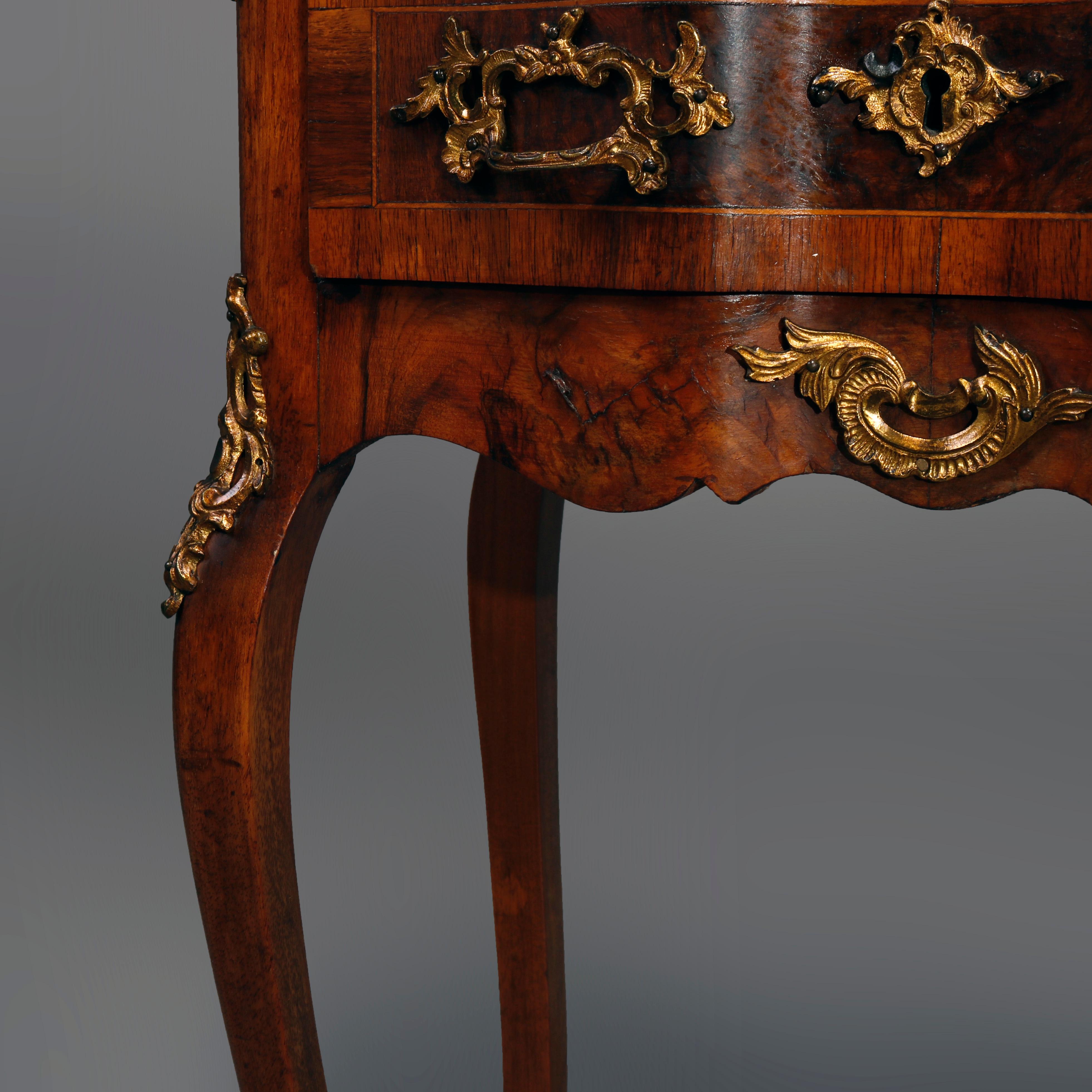 An antique French Rococo side stand in the manner of Francois Linke offers kingwood construction with shaped top surmounting serpentine case having double crossbanded drawers with burl insets and foliate cast ormolu mounts over shaped skirt, raised