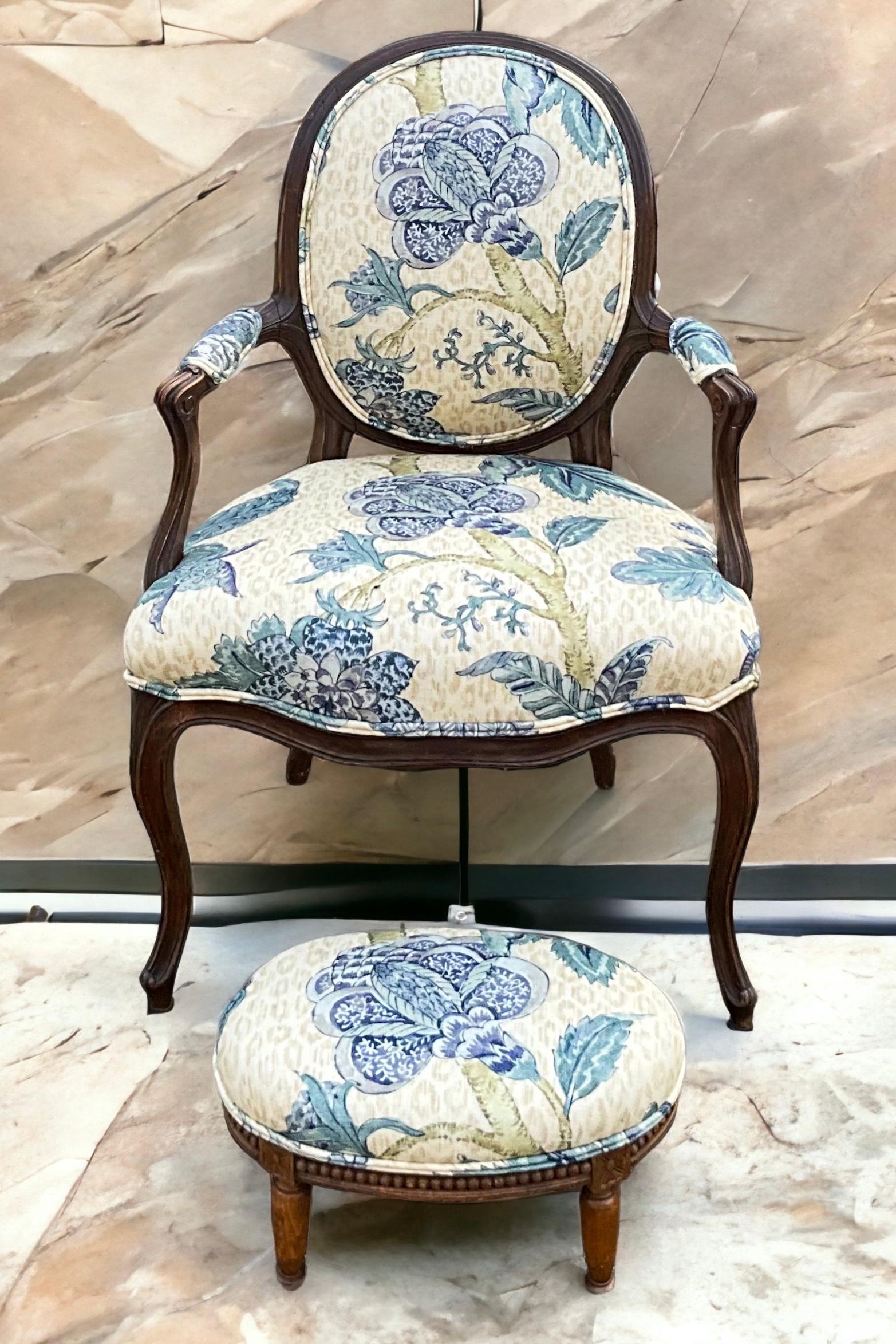 This is an early 20th century French carved fruitwood bergere  chair newly upholstered in a blue floral with neutral leopard background. The fabric is linen. The stool came with the chair but is not quite as old as the chair nor the same wood. It